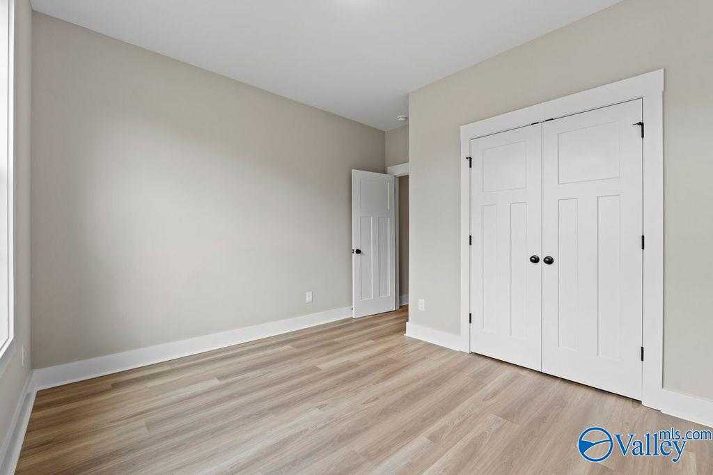 Bright secondary bedroom with beige walls, white paneled doors, and light wood flooring in Evermore Homes The Oxford, Owens Cross Roads, AL