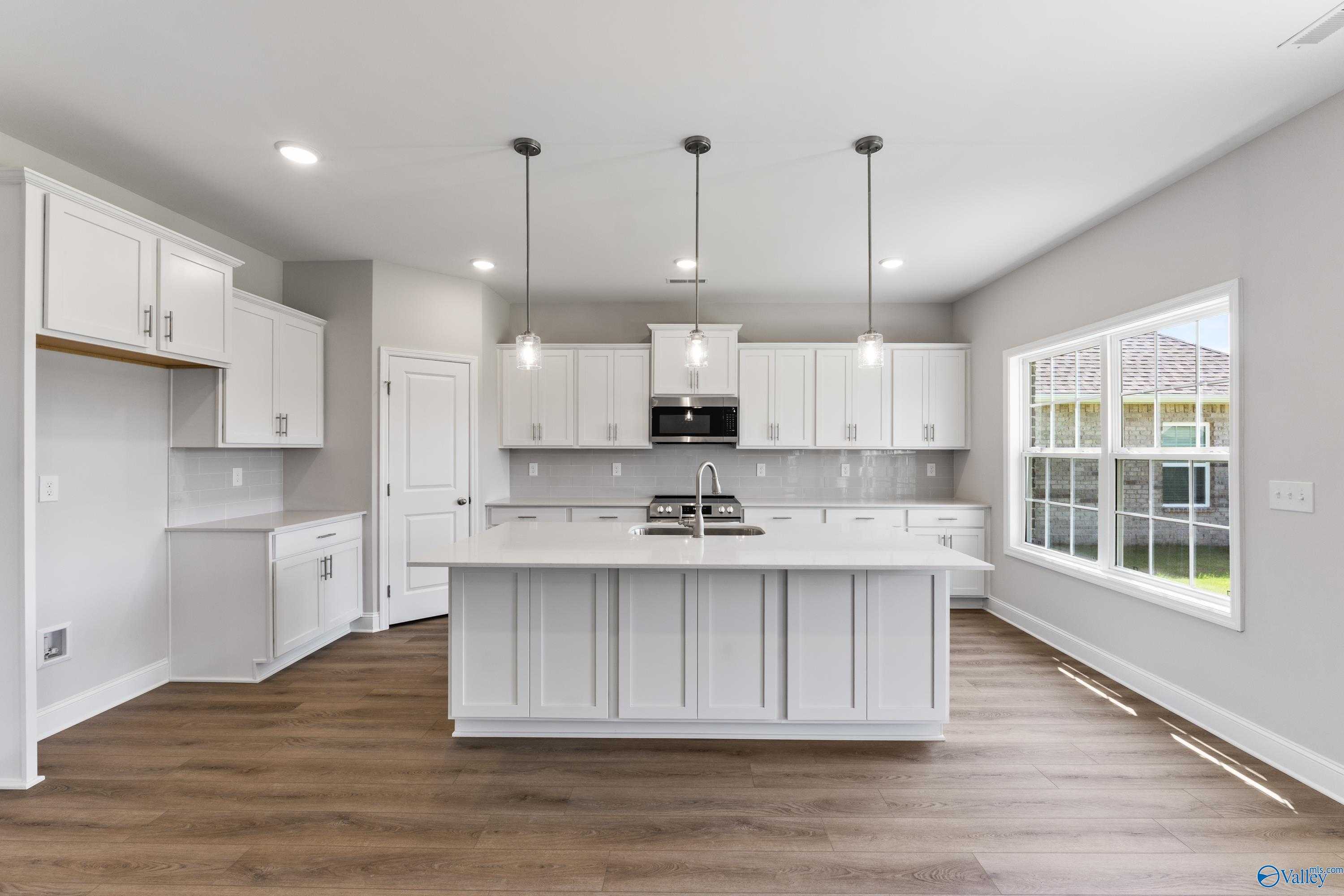 Modern white kitchen with large island, stainless appliances, hardwood floors in Davidson Homes Madison A, Toney AL