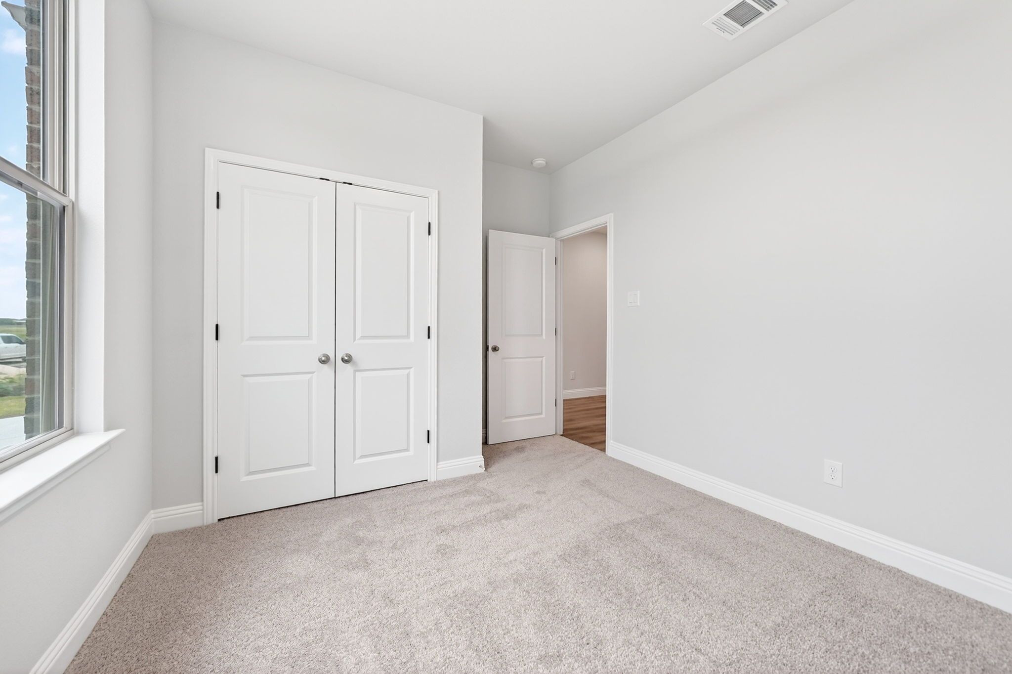 Bright bedroom with plush carpet and closet space in The Redbud floor plan by Davidson Homes in Josephine, Texas.