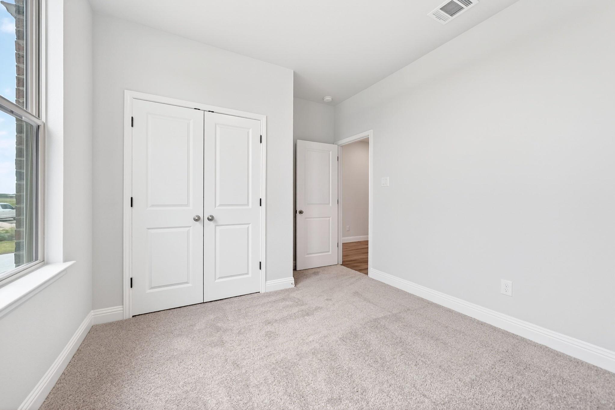 Bright bedroom with plush carpet and closet space in The Redbud floor plan by Davidson Homes in Josephine, Texas.