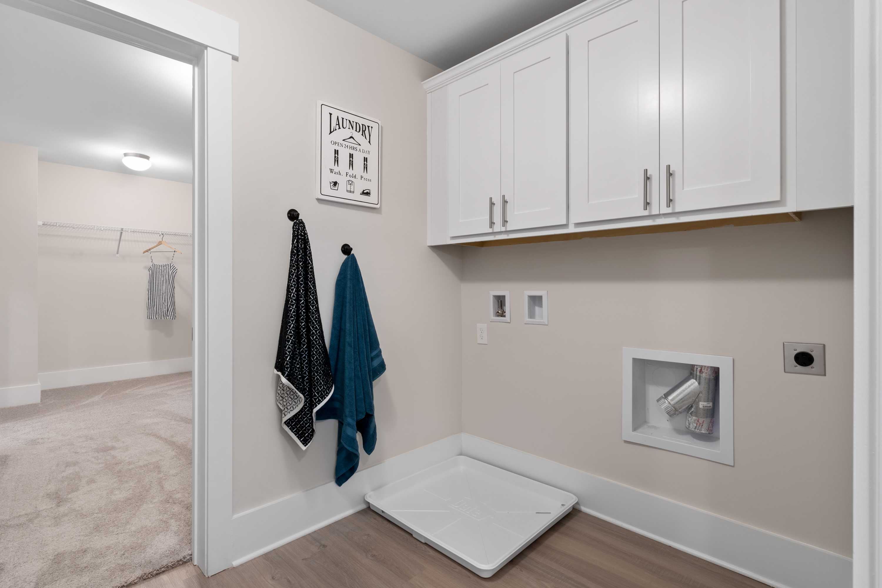 Spacious laundry room in The Chelsea A home with white shaker cabinets, hanging towels, washer dryer hookups, and pet bed on hardwood floor