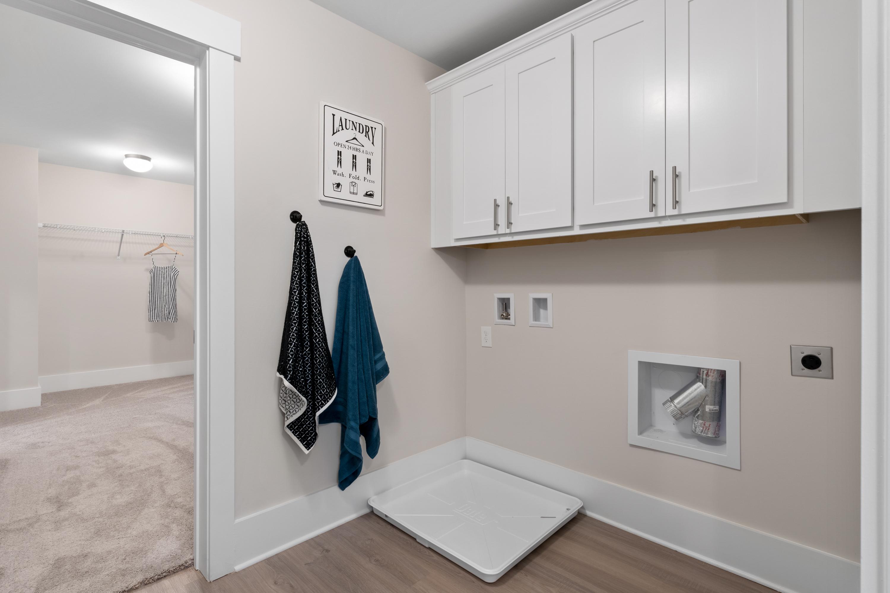 Spacious laundry room in The Chelsea A home with white shaker cabinets, hanging towels, washer dryer hookups, and pet bed on hardwood floor
