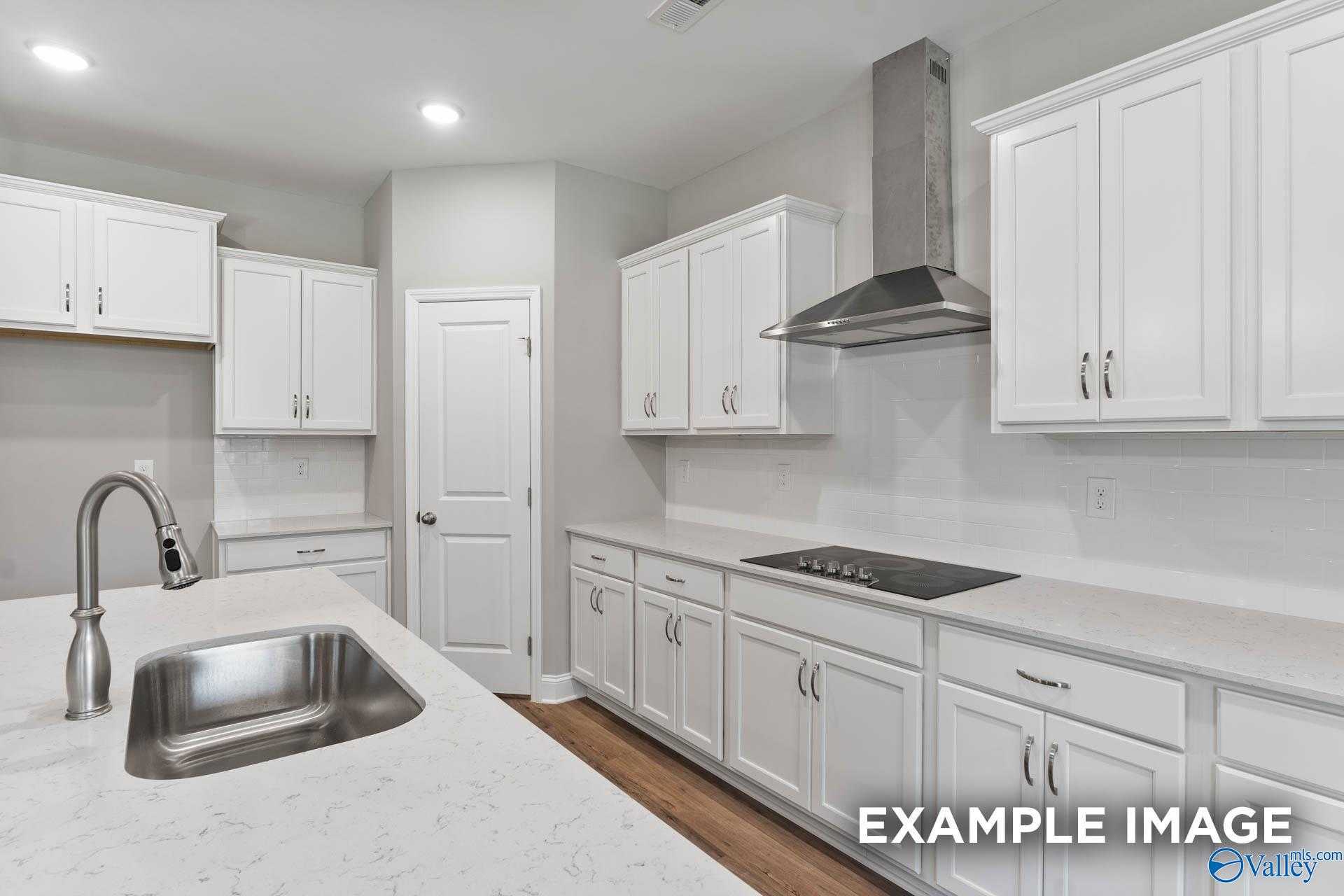 Modern white shaker kitchen with quartz island, stainless range hood, and hardwood floors in Davidson Homes The Rockford D, Hazel Green AL