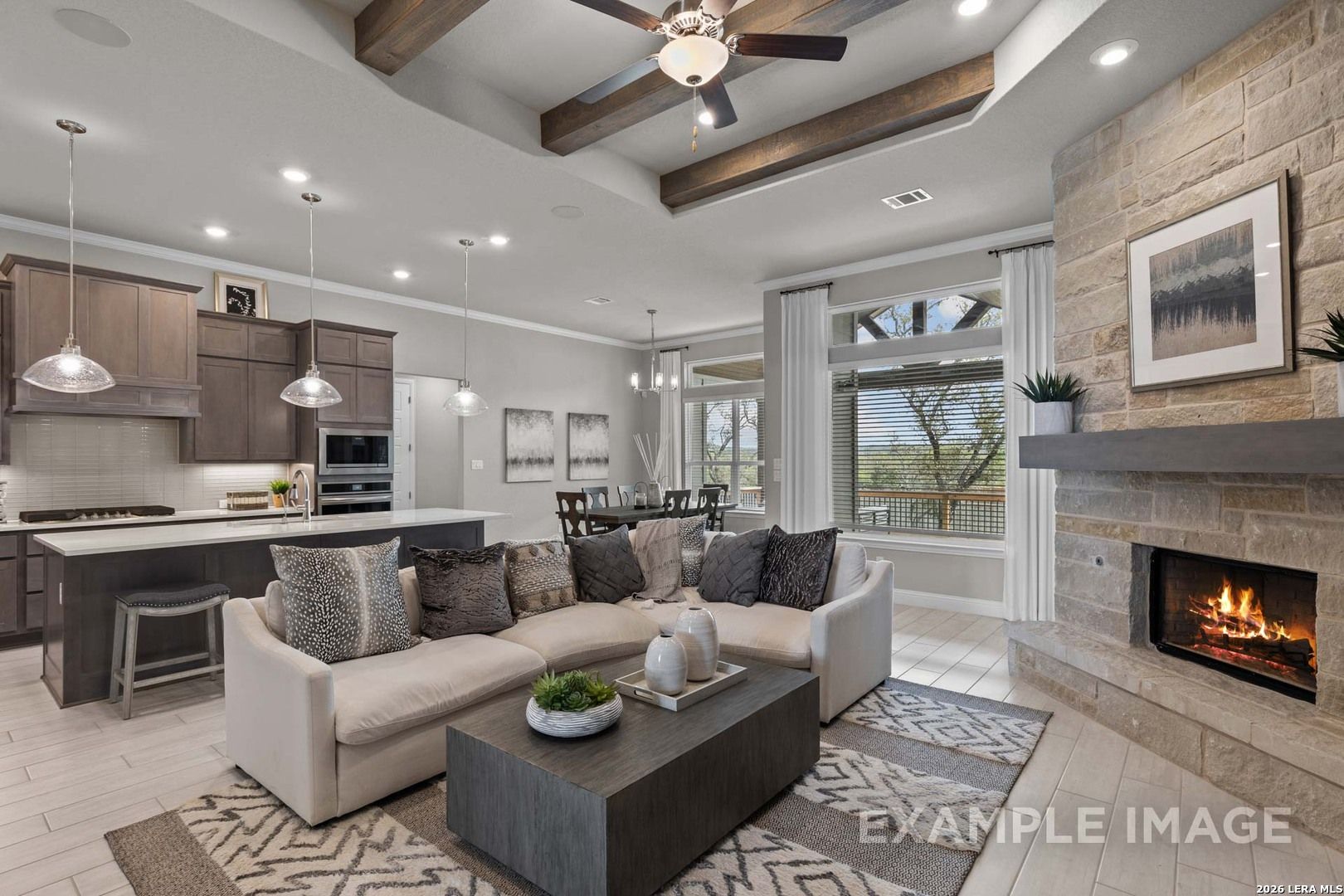 Open-concept living room with stone fireplace, wood beams, and kitchen in The Garner C plan at Potranco Oaks, Castroville.