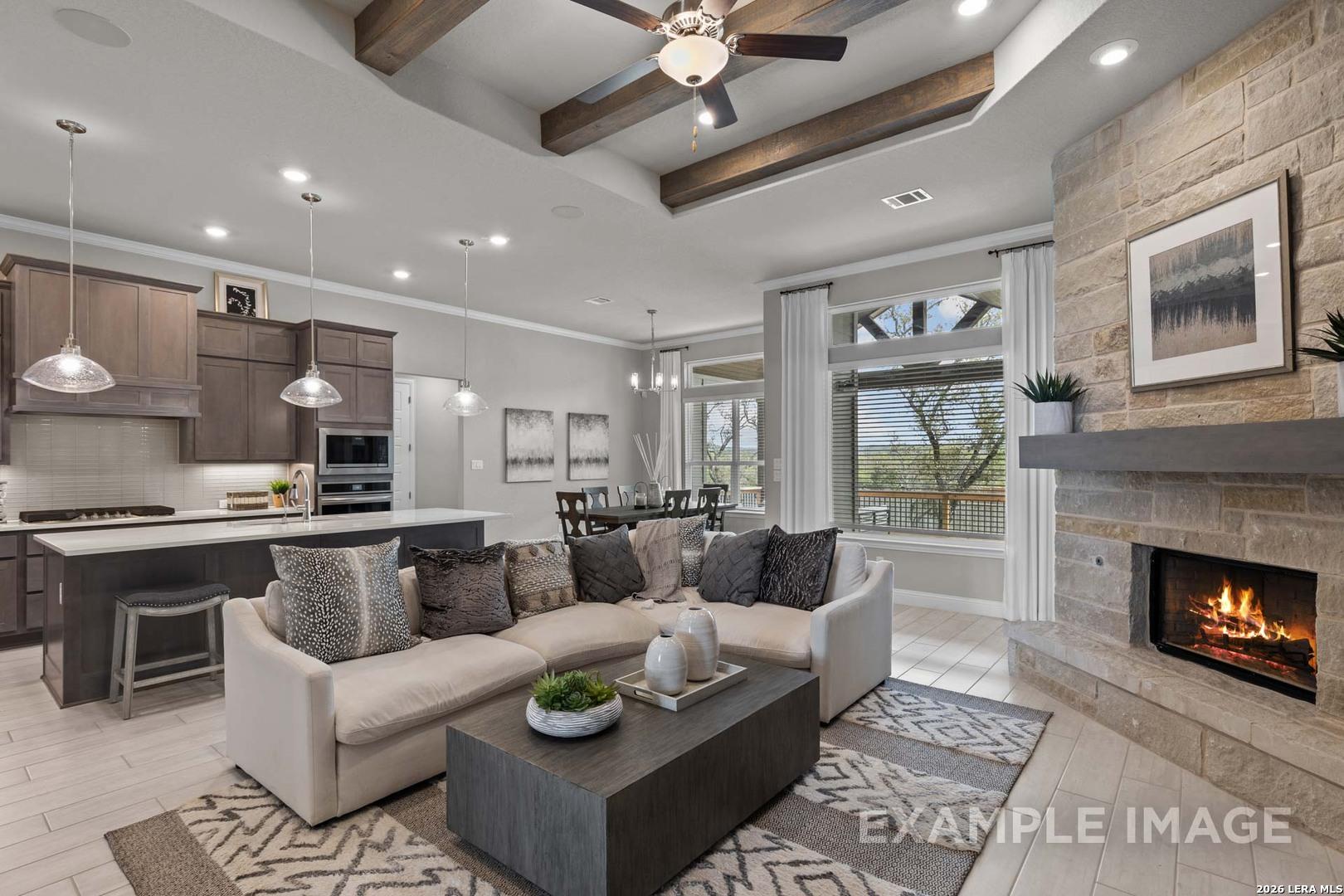 Open-concept living room with stone fireplace, wood beams, and kitchen in The Garner C plan at Potranco Oaks, Castroville.