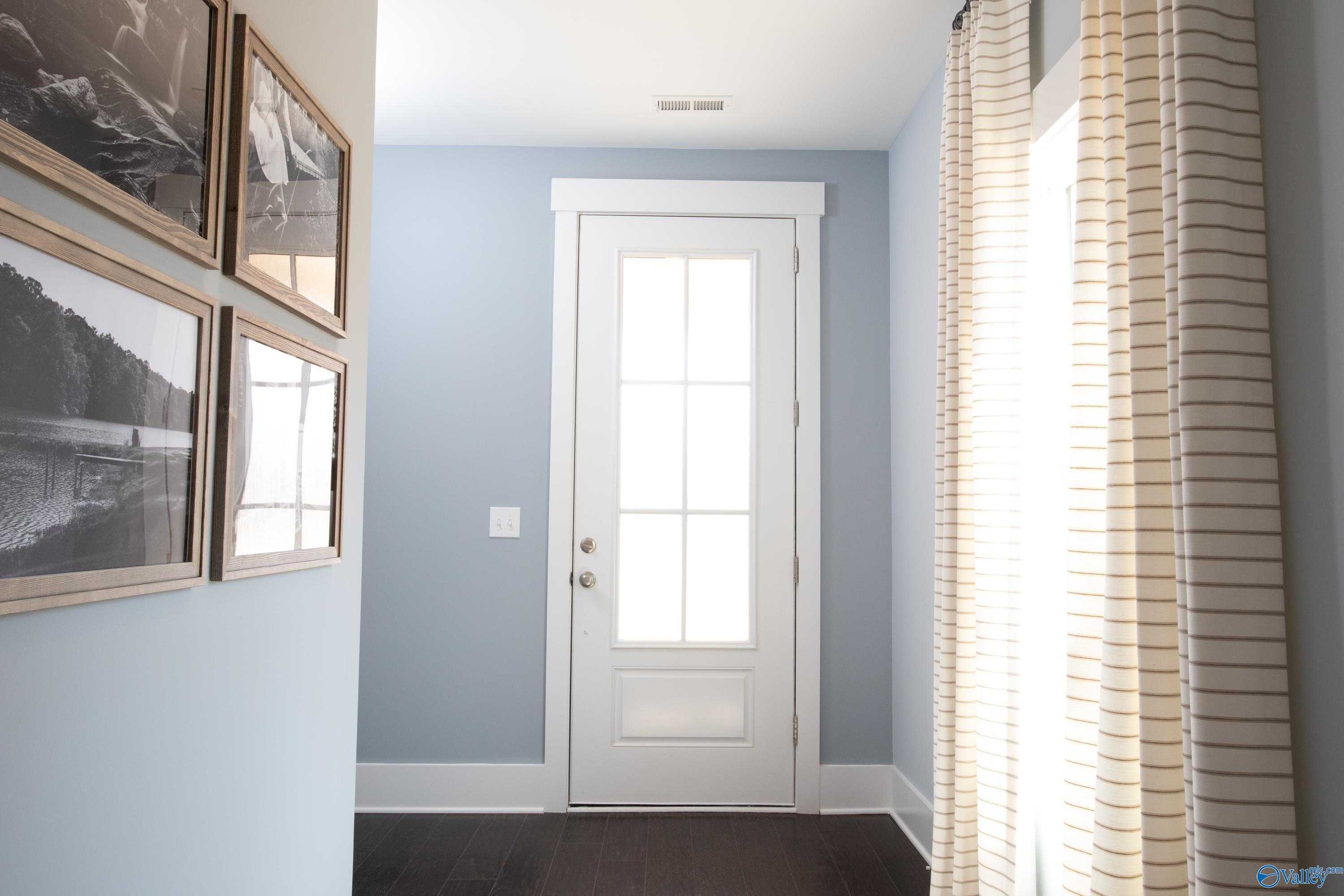 Bright hallway with pale blue walls, white glass-paneled door, hardwood floors, and framed art in Davidson Homes The Covington C, Decatur, AL