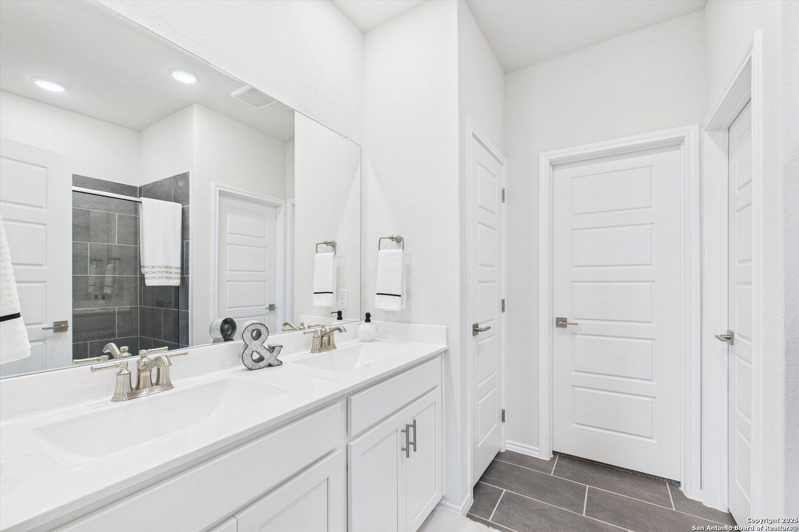 Modern master bathroom with double vanity sinks, frameless glass shower, and white shaker cabinets in Davidson Homes The Asheville K, San Antonio
