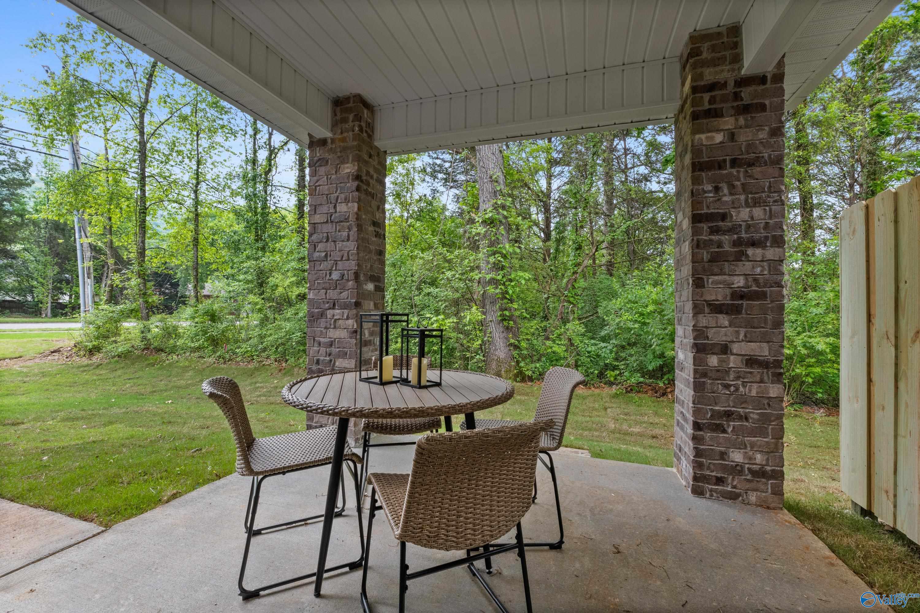 Covered back patio with round wicker table, chairs, and lanterns overlooking lush wooded backyard in Davidson Homes The Camden, Huntsville, Alabama