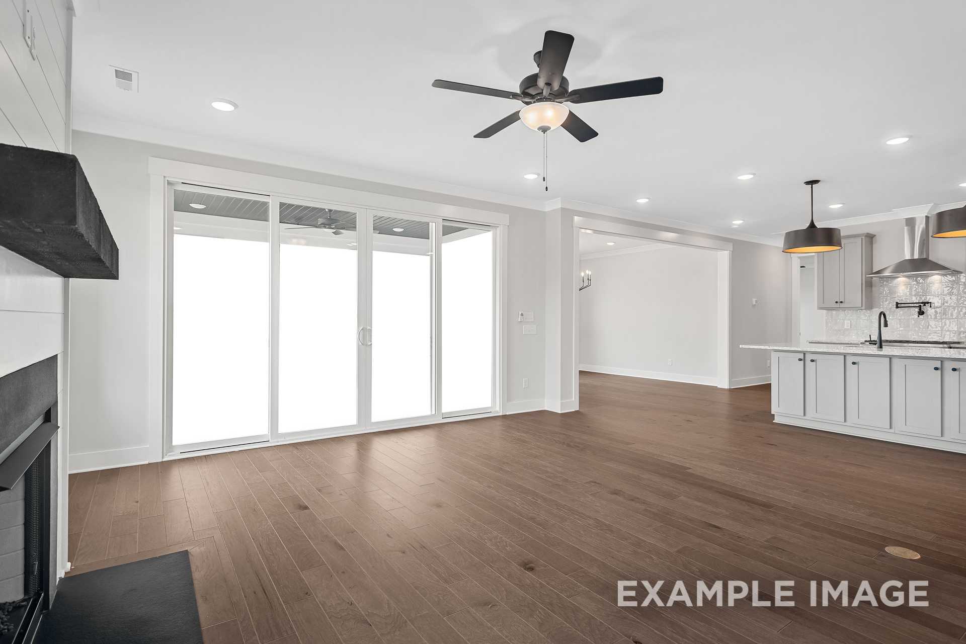 Spacious open-concept living room in The Hathaway with shiplap fireplace, large sliding doors, ceiling fan, and adjacent modern kitchen featuring white cabinets and island