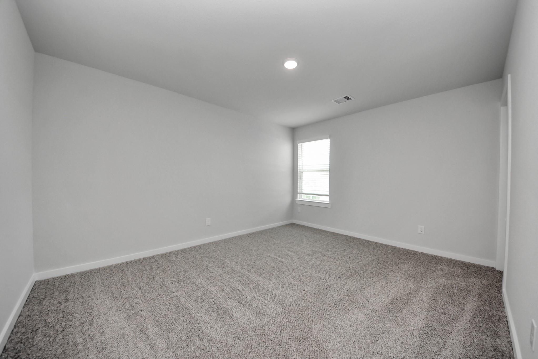 Bright empty bedroom with neutral carpet and white walls in Davidson Homes The San Marcos E floor plan, Emberly, Beasley, Texas