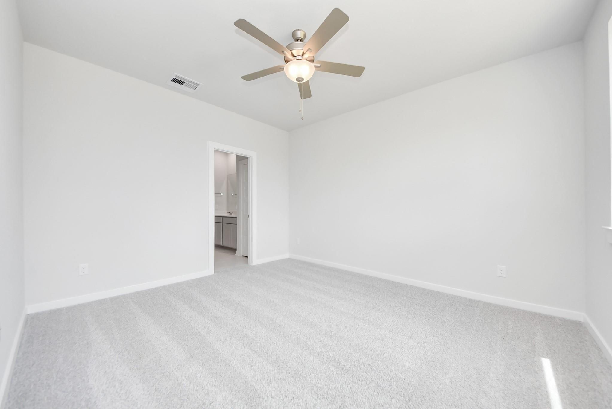 Spacious bedroom with plush carpet and ceiling fan in The Blanco F floor plan at Spring Branch Crossing, Conroe, Texas.
