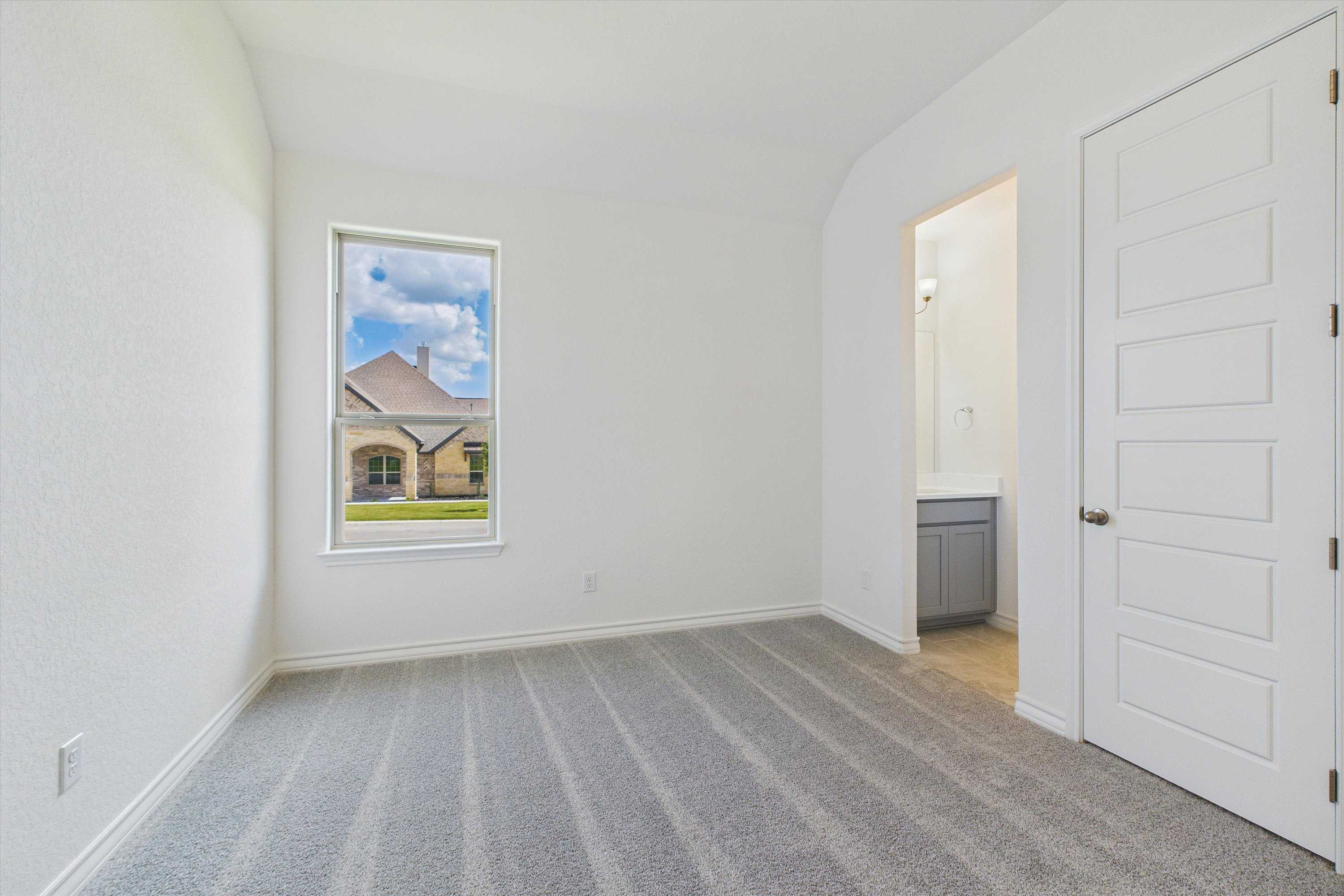 Bright secondary bedroom with window view of beige home and green lawn in Davidson Homes Summerlin C, Castroville, Texas