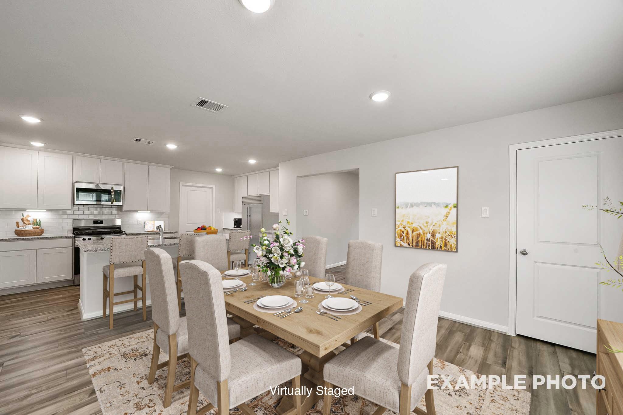 Open-concept dining area with wooden table, upholstered chairs, and floral centerpiece beside modern white kitchen in Davidson Homes The Tierra B, Beasley Texas