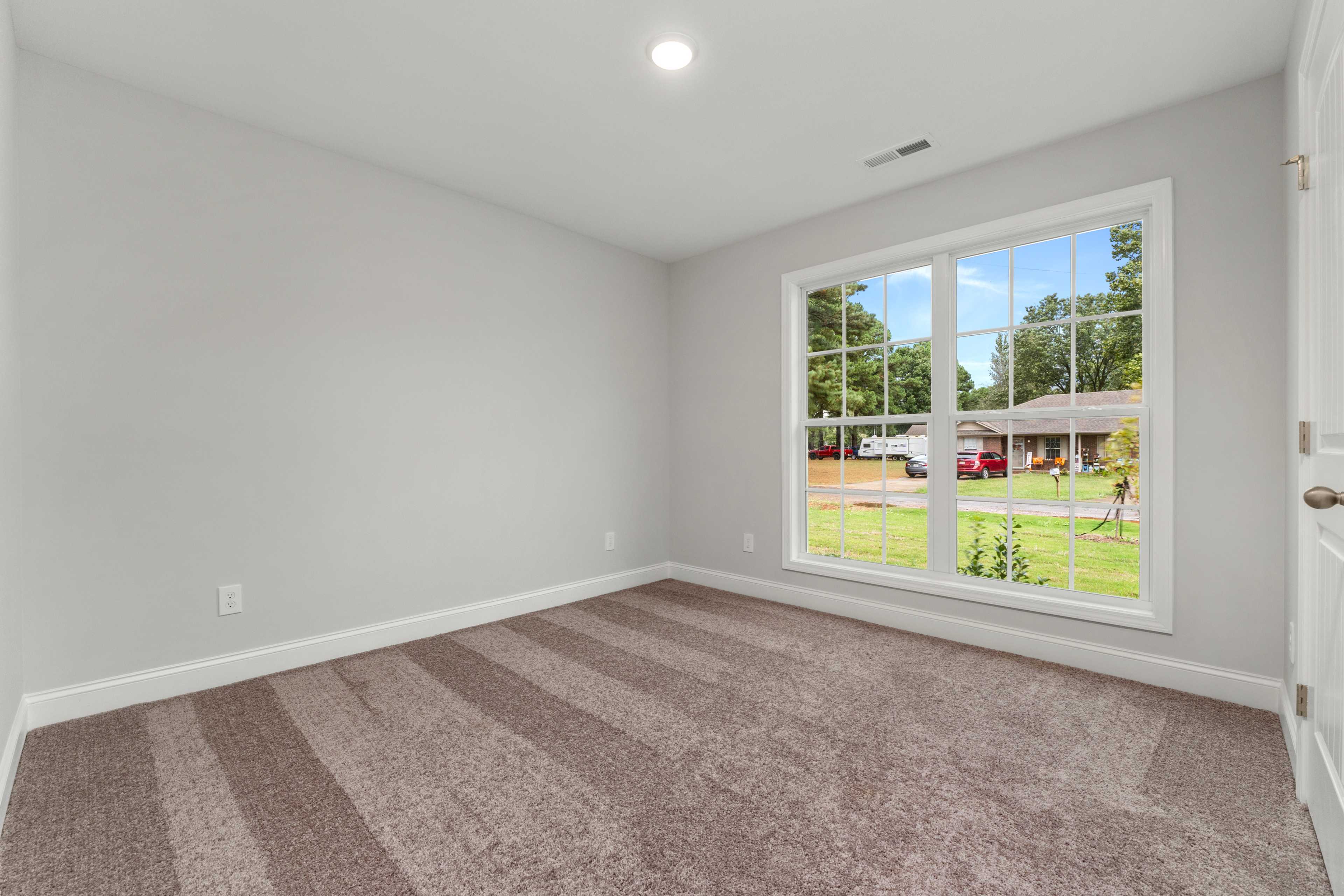 Spacious empty bedroom at Collins Lane in Meridianville AL with gray walls, striped carpet, and large window overlooking green yard