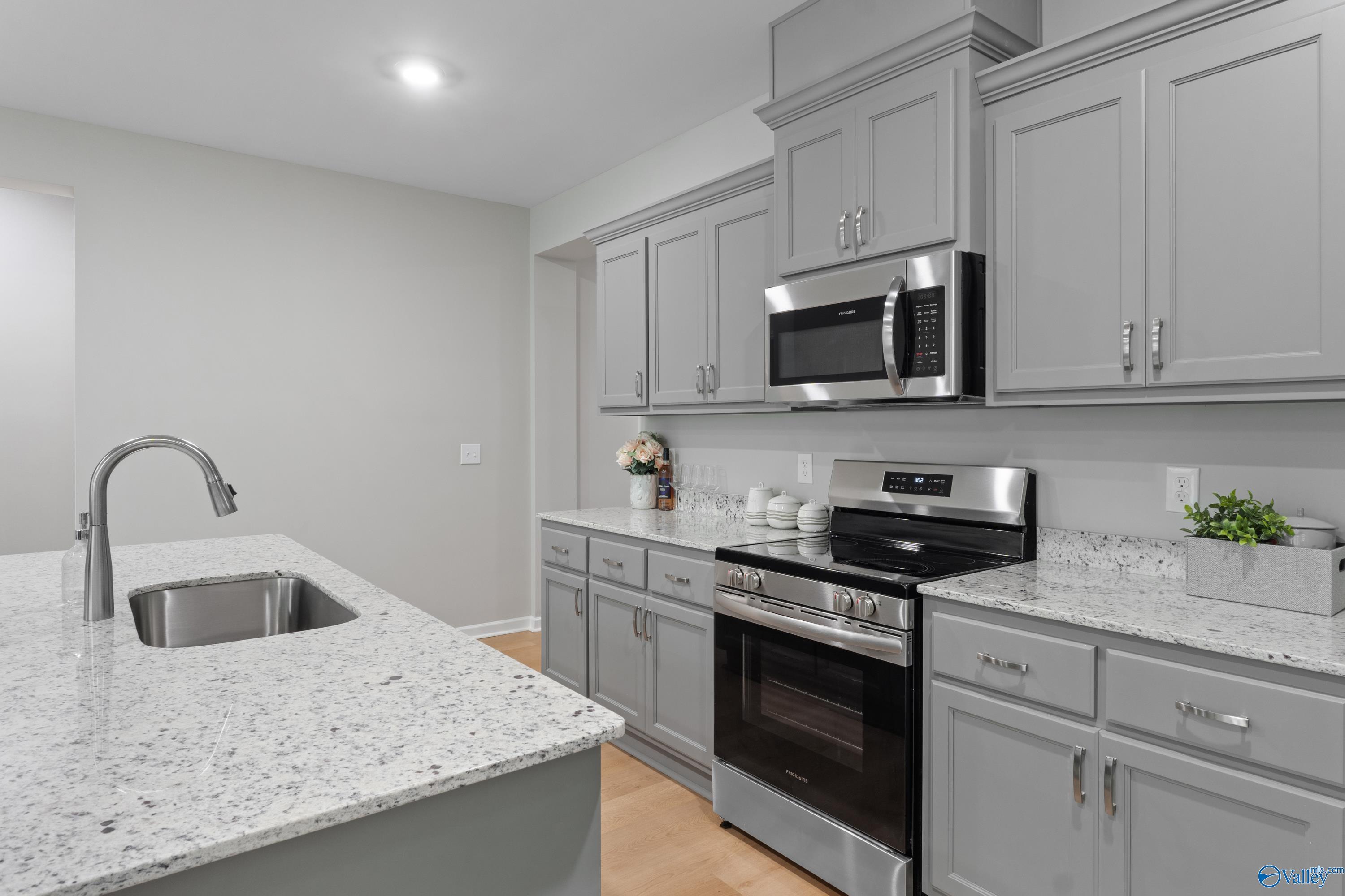 Modern gray shaker kitchen with quartz island, stainless microwave, oven in The Luna 4-bedroom home, Hazel Green, AL