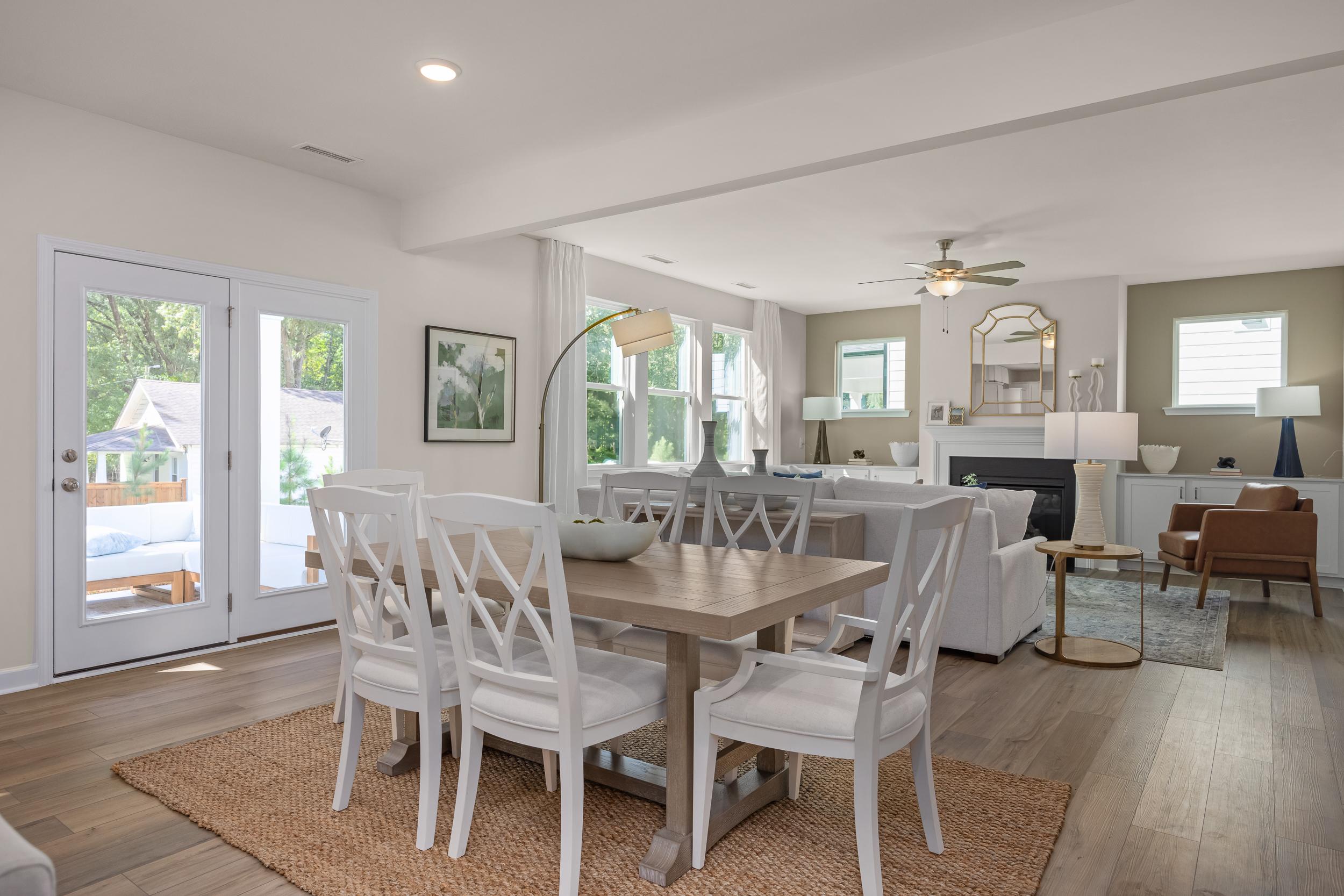 Spacious open-concept living and dining area in The Hickory II featuring wooden table, white chairs, fireplace, and large windows