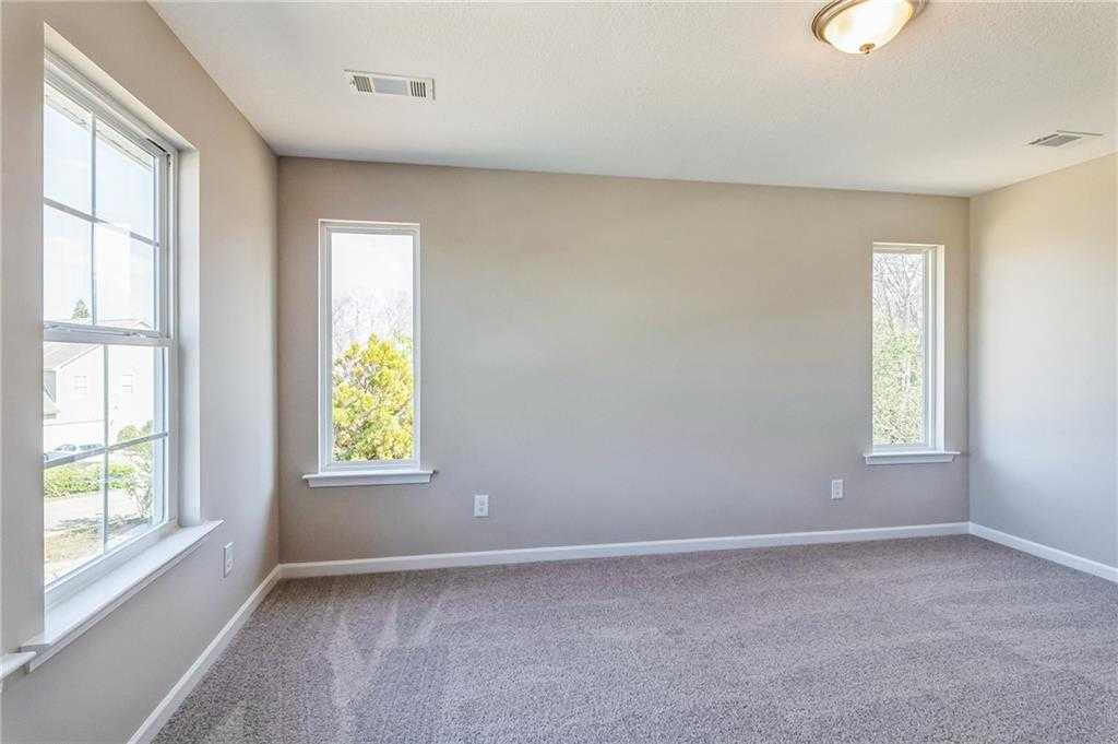 Bright empty bedroom with large windows, beige walls, and carpeted floor in Evermore Homes The Stella, Ivy Glen, Perry, Georgia