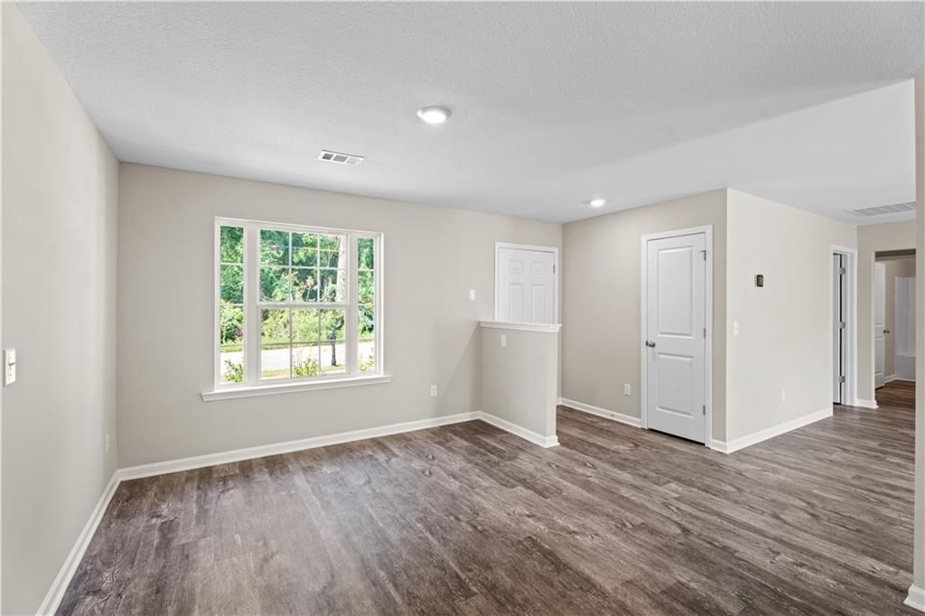 Bright empty living room with beige walls, large window to greenery, luxury vinyl plank floors in Davidson Homes The Washington, Phenix City