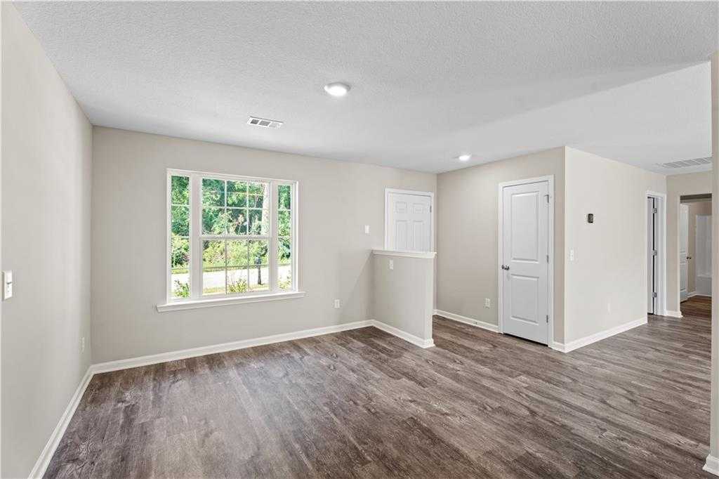 Bright empty living room with beige walls, large window to greenery, luxury vinyl plank floors in Davidson Homes The Washington, Phenix City