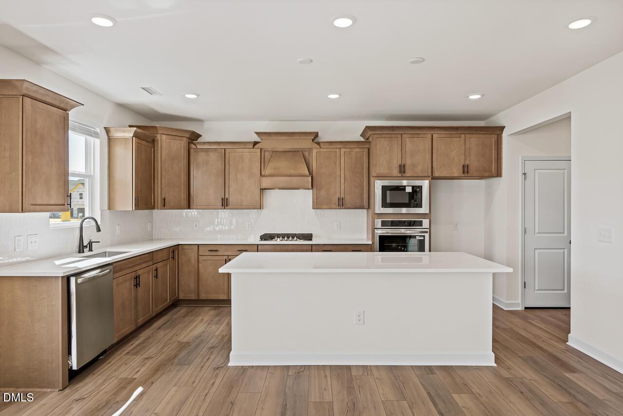 Modern kitchen with white island, wood cabinets, and stainless appliances in Davidson Homes' Hickory II B plan, Lillington, NC