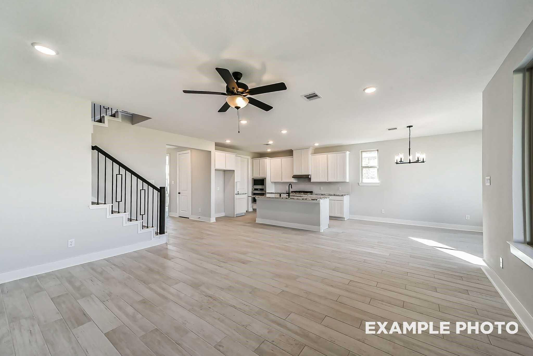 Open-concept kitchen with white island, cabinets, ceiling fan, and black staircase in Davidson Homes The Philip C, Rosharon, Texas