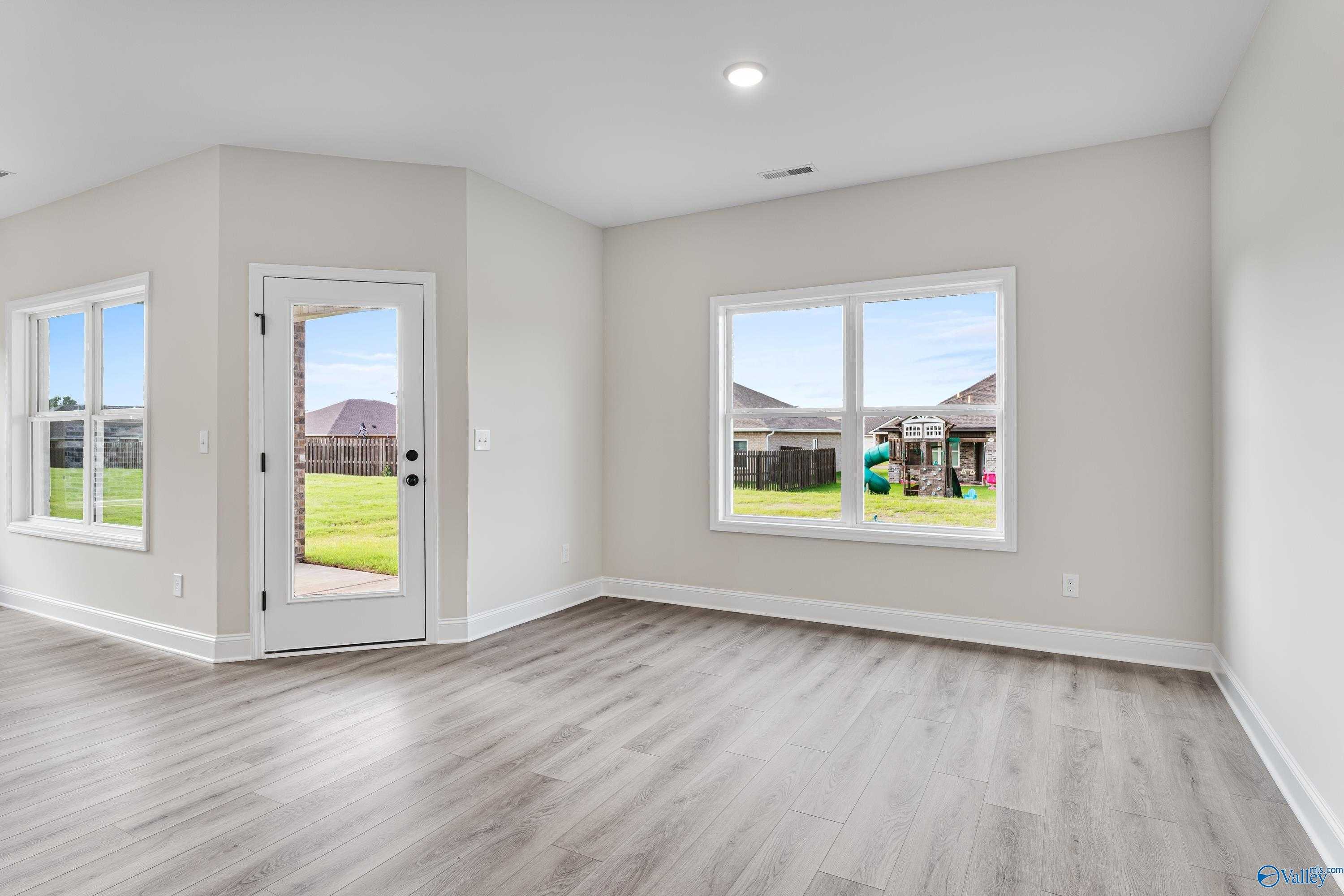 Bright living room with beige walls, luxury vinyl flooring, large windows overlooking fenced backyard and playset in Davidson Homes Franklin B, Hazel Green AL