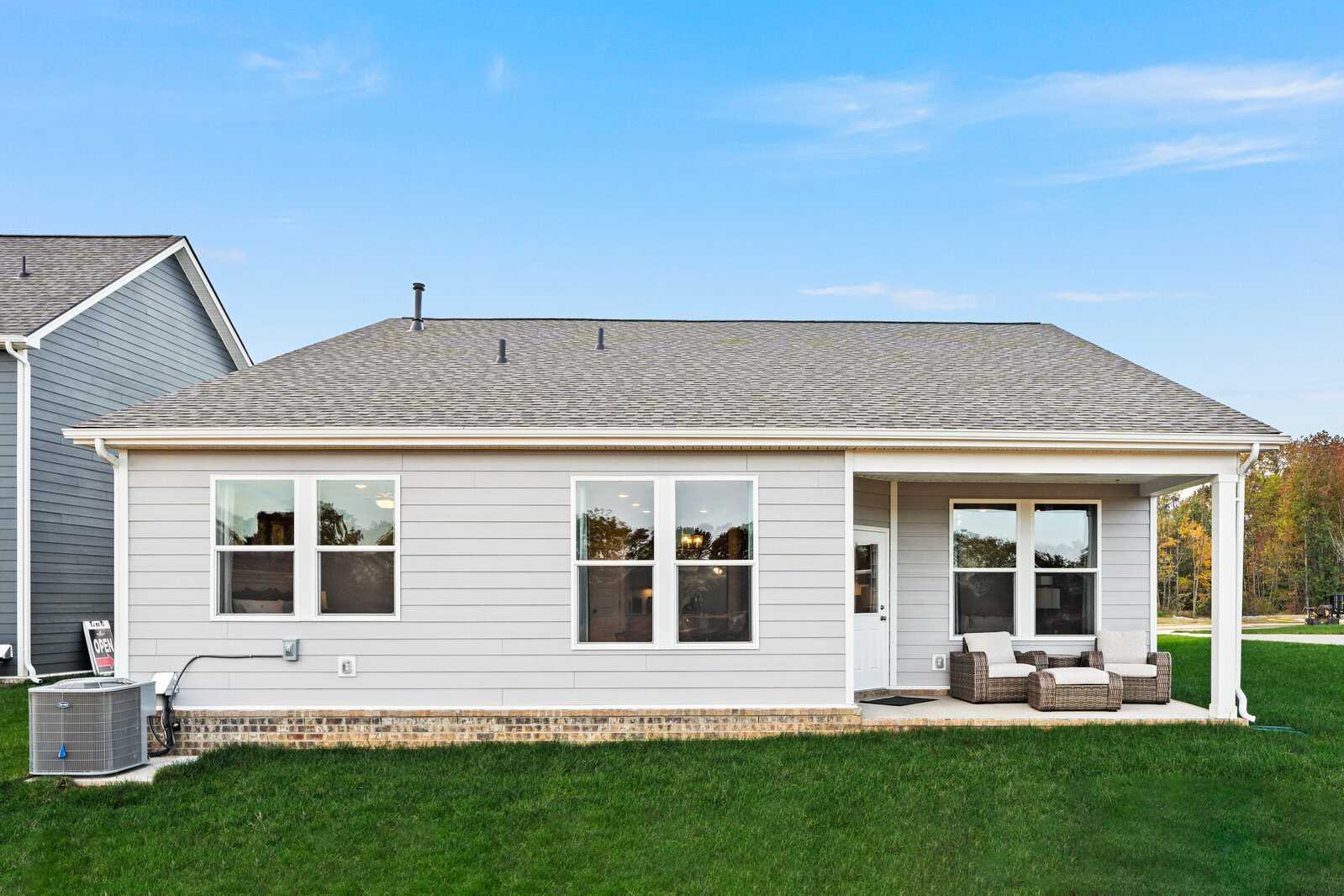Gray-sided ranch home exterior at Sage Farms in White House Tennessee with covered porch, large windows, and patio seating on green lawn