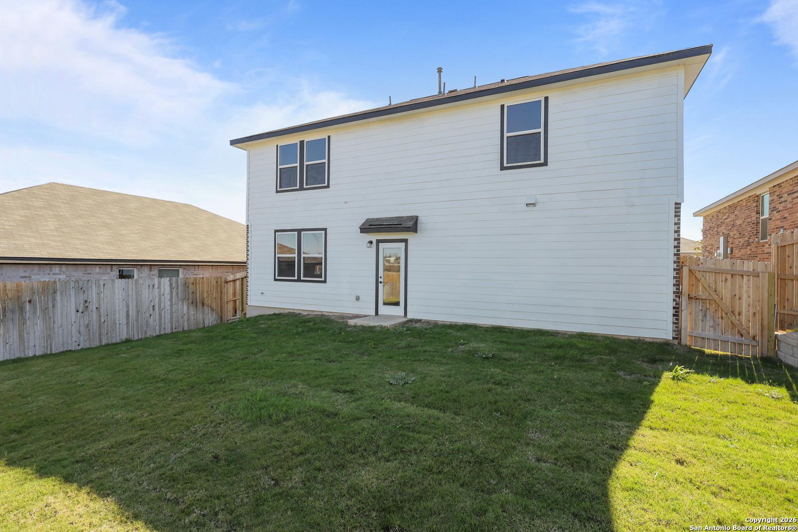 Two-story white home rear with covered patio, lush green backyard, and wooden fence in Comanche Ridge, San Antonio, Texas - Davidson Homes The Murray K