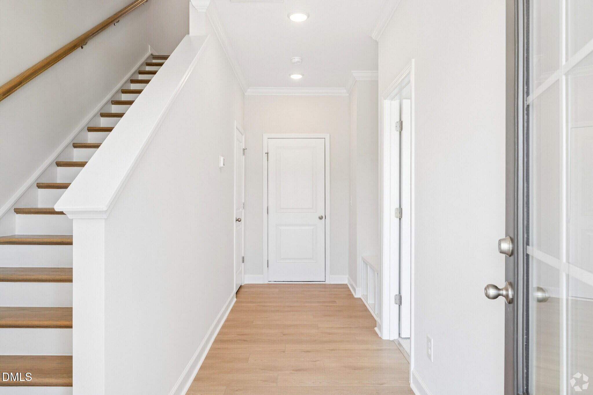 Bright entryway foyer with hardwood floors, white staircase, and crown molding in Davidson Homes The Mitchell townhome, Knightdale, NC