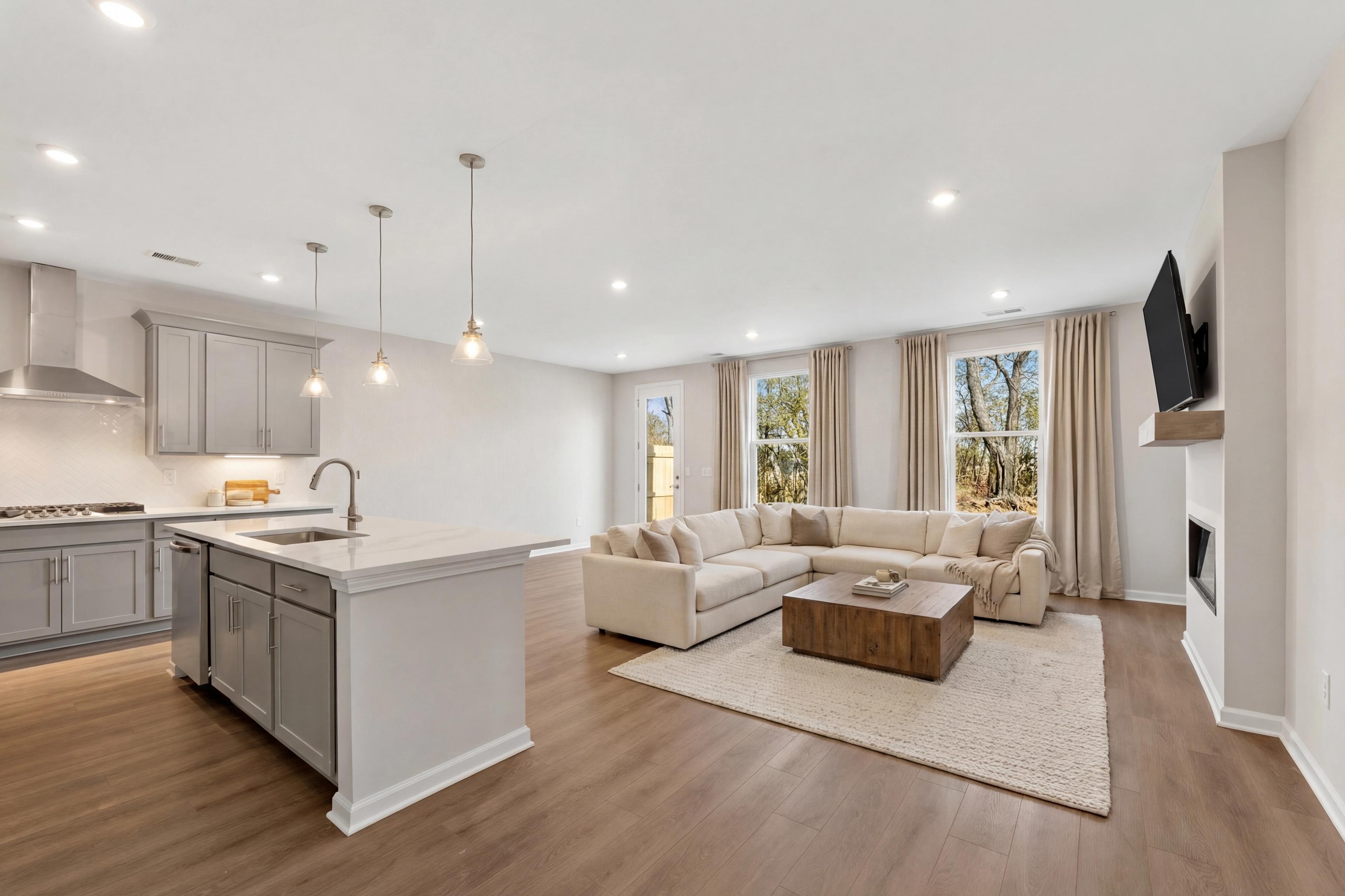 Open-concept kitchen and living room at Lake Shore in Winder Georgia with quartz island, hardwood floors, L-shaped sofa, and gas fireplace