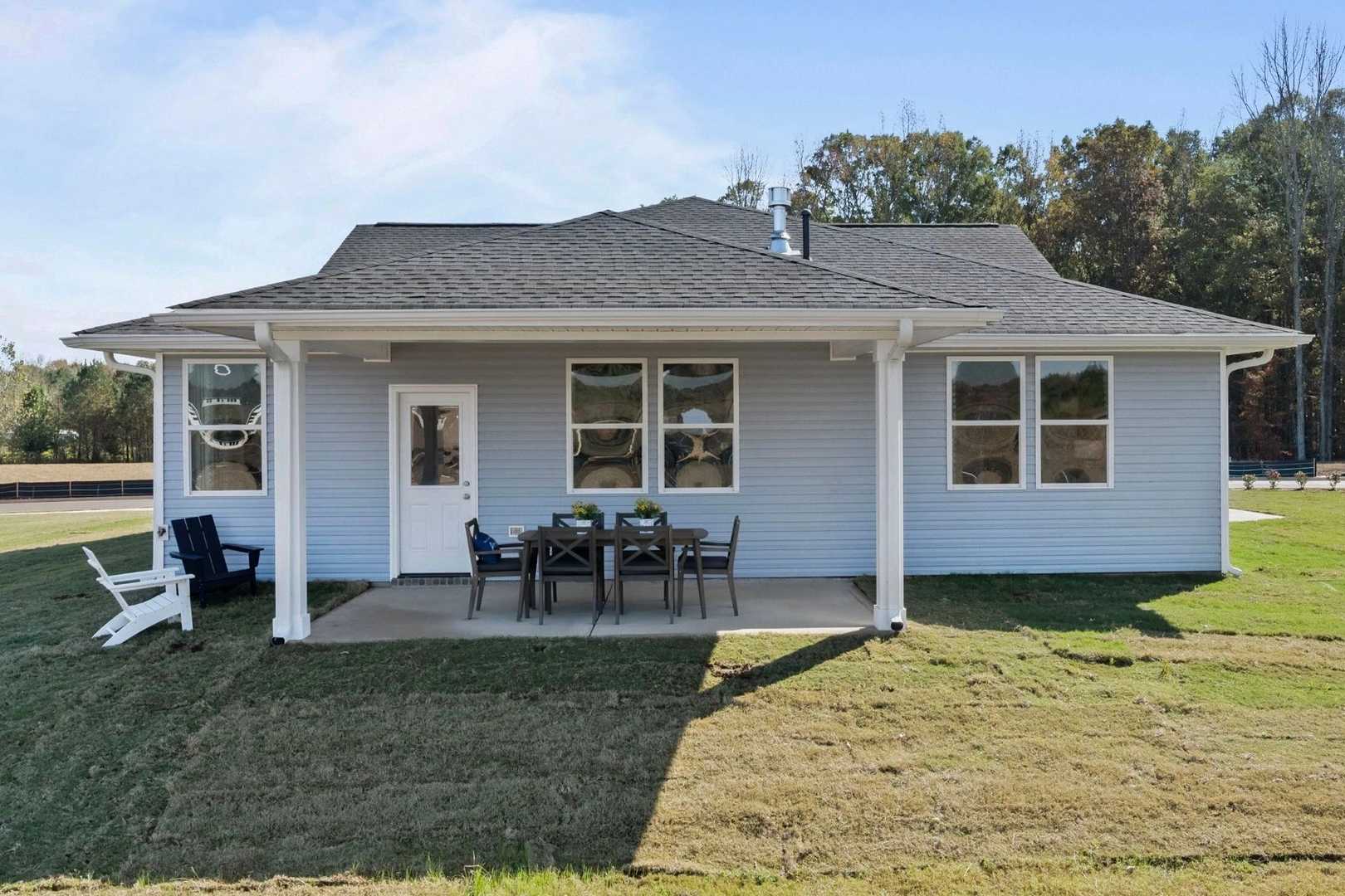 Rear view of light blue craftsman home at Bailey Park in Fayetteville TN with covered porch, patio seating, and lush lawn