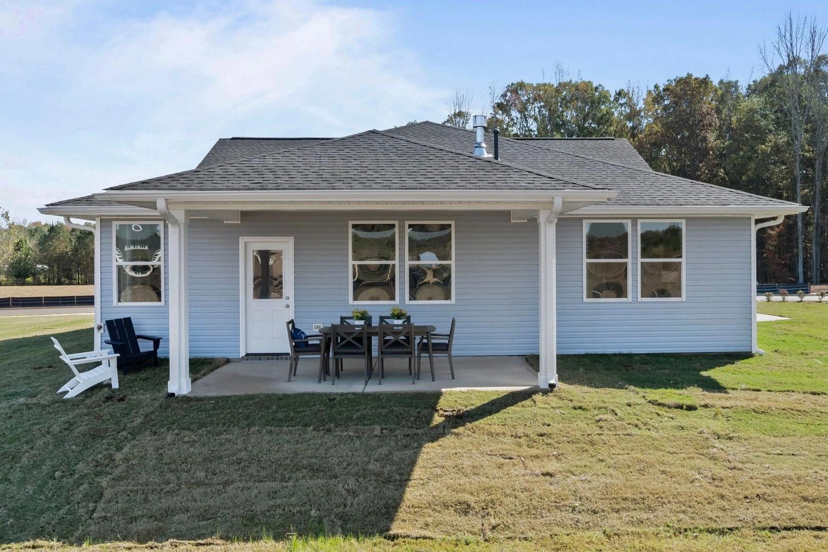 Rear view of light blue craftsman home at Bailey Park in Fayetteville TN with covered porch, patio seating, and lush lawn