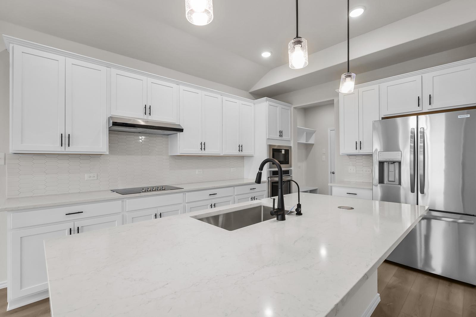 Modern white kitchen in The Sequoia C featuring a quartz island, stainless steel appliances, and pendant lighting.