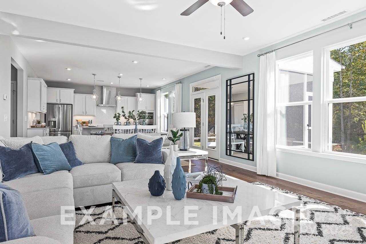 Modern open-concept living room with blue sectional sofa, wooden coffee table, and adjacent white kitchen in Davidson Homes The Hemlock A, Belmont, NC