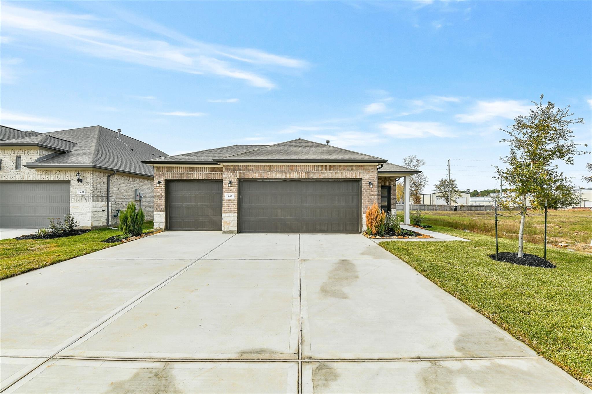 Modern brick single-story home with 3-car garage, wide driveway, and lush landscaping in Windmill Estates, Magnolia, Texas