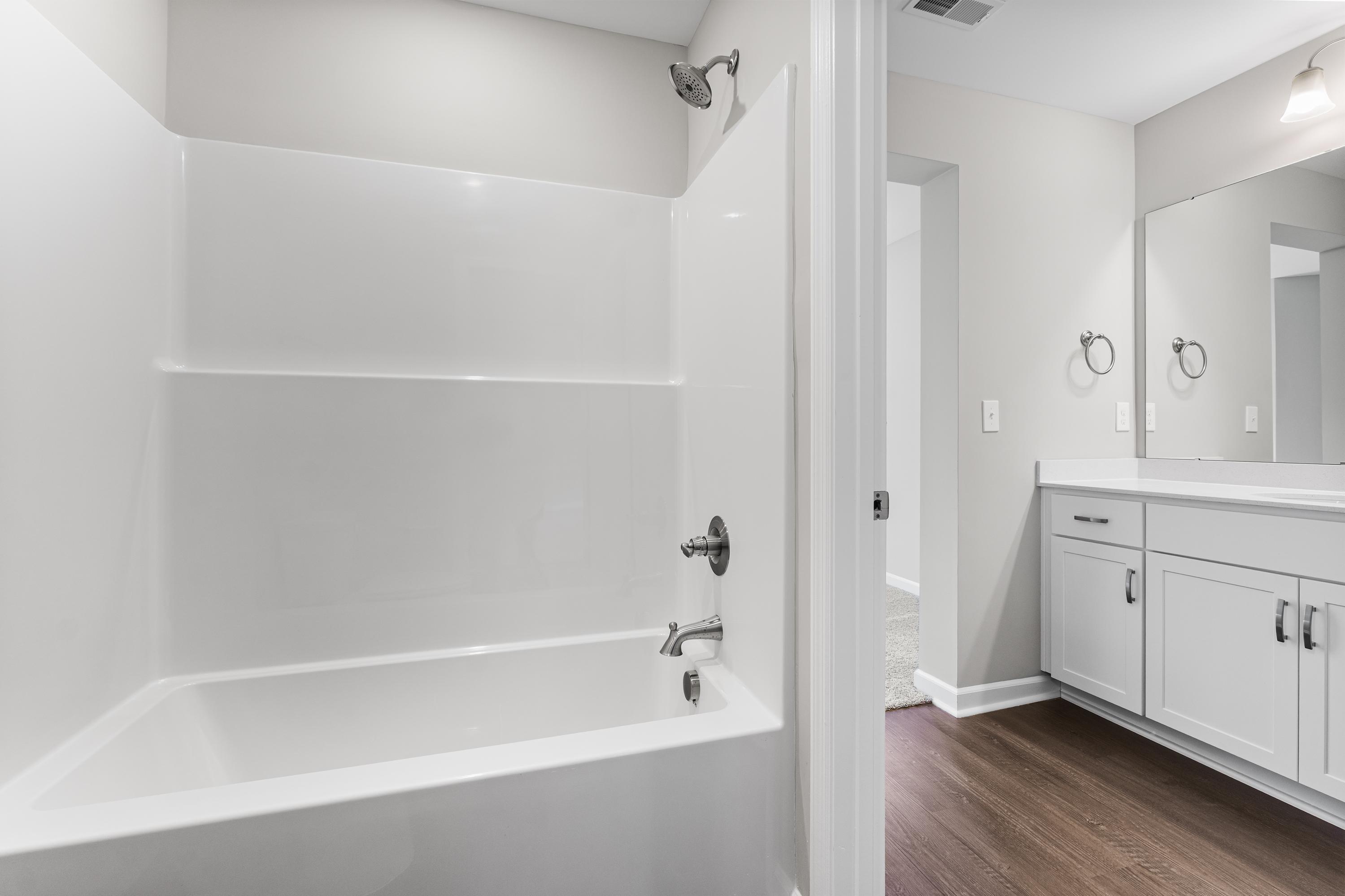 Spacious master bathroom in The Avalon D with white bathtub, glass shower, double vanity, mirrors, and hardwood floors