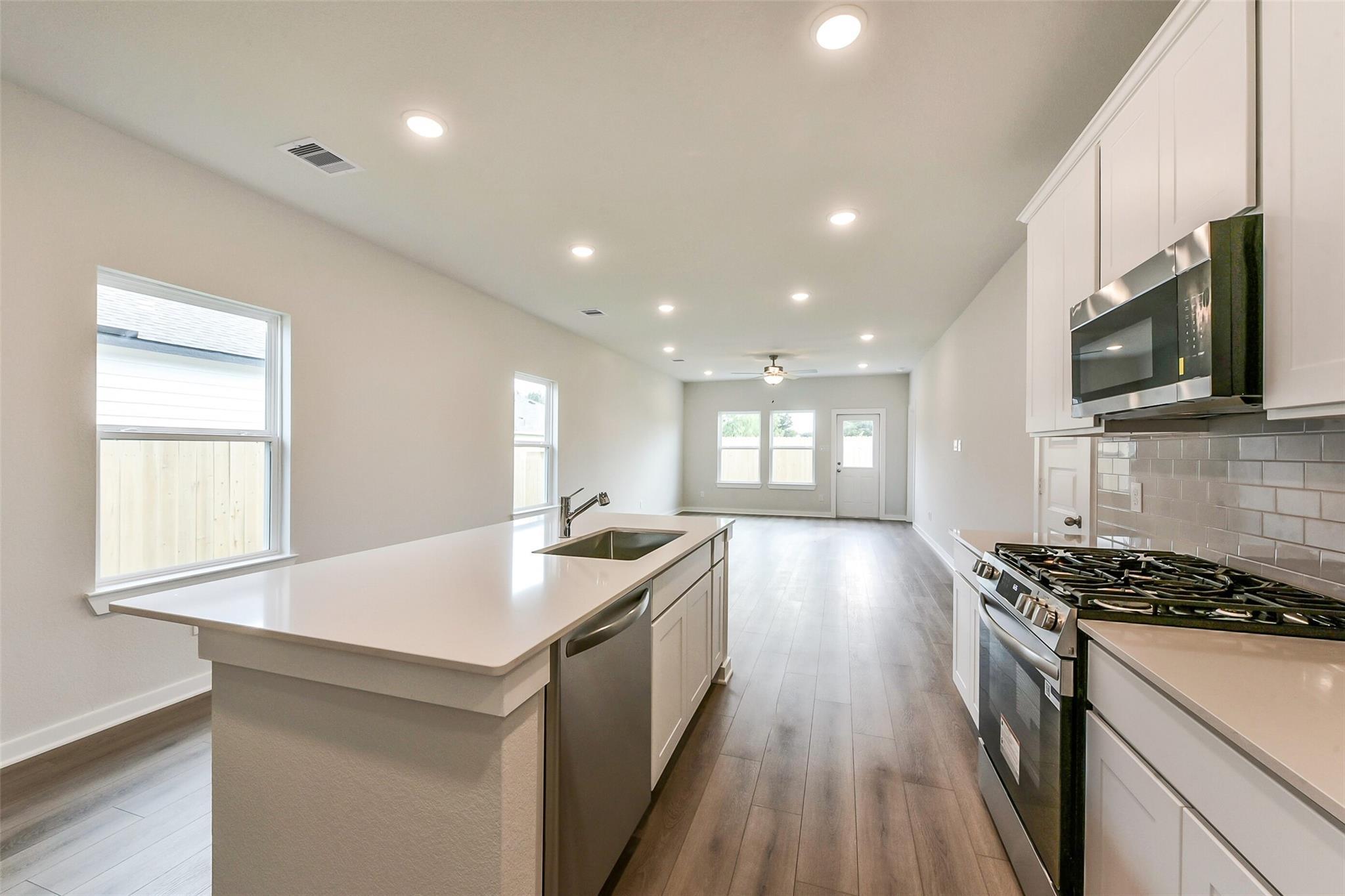 Modern open kitchen with white cabinets, stainless appliances, quartz island, and subway tile in The Frio G home, Dayton TX