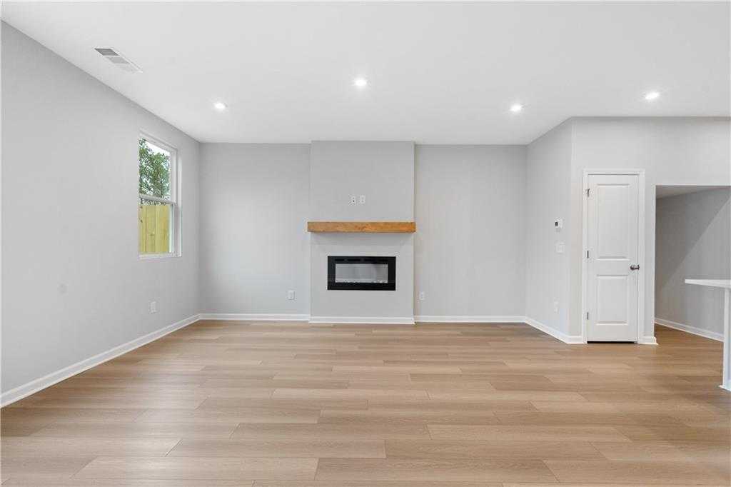 Modern living room with gas fireplace, wood mantel, and large window in Davidson Homes The Durant A, Emerson, Georgia