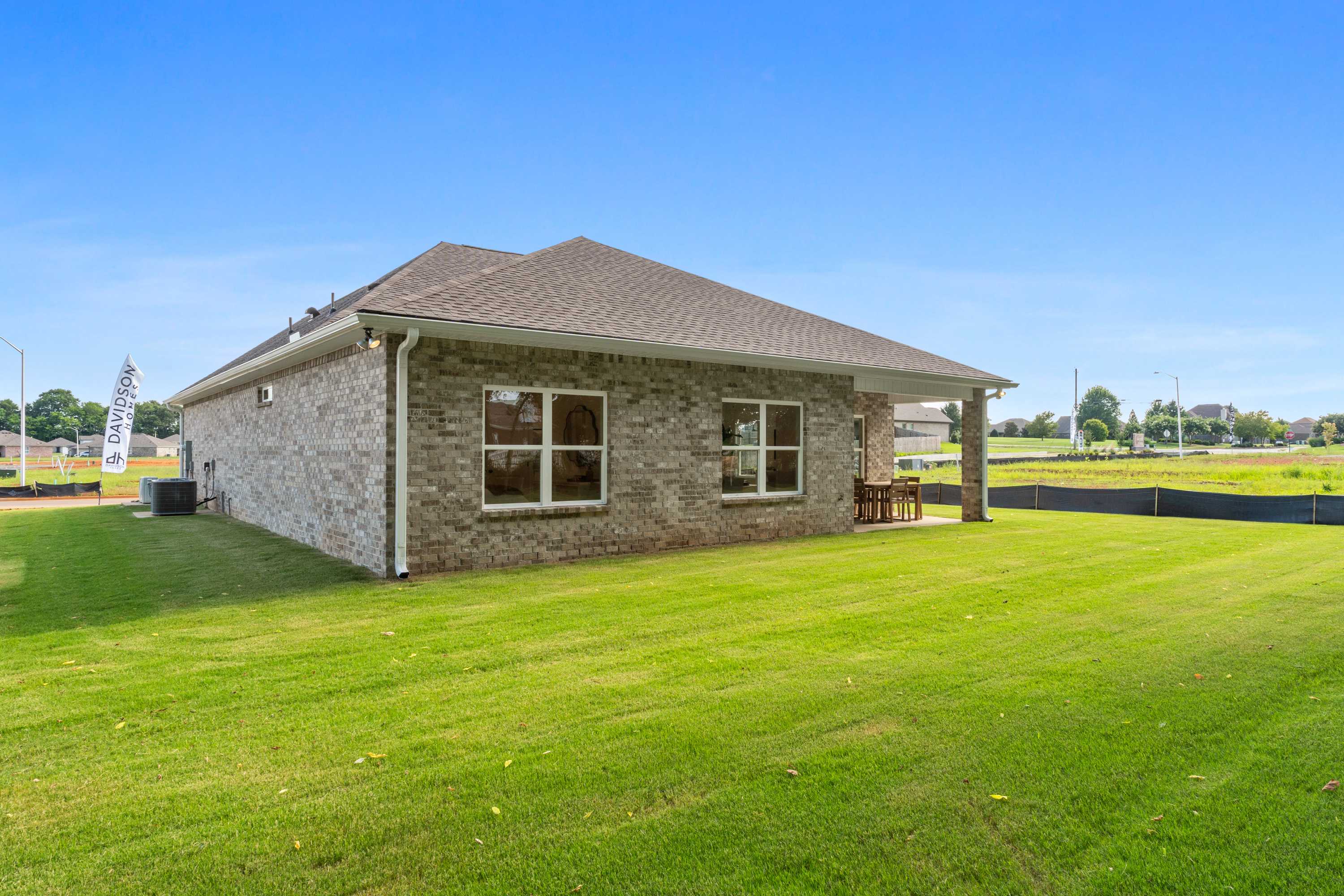Brick home side exterior at Lynn Meadows in Meridianville Alabama with covered patio, large windows, and lush green lawn