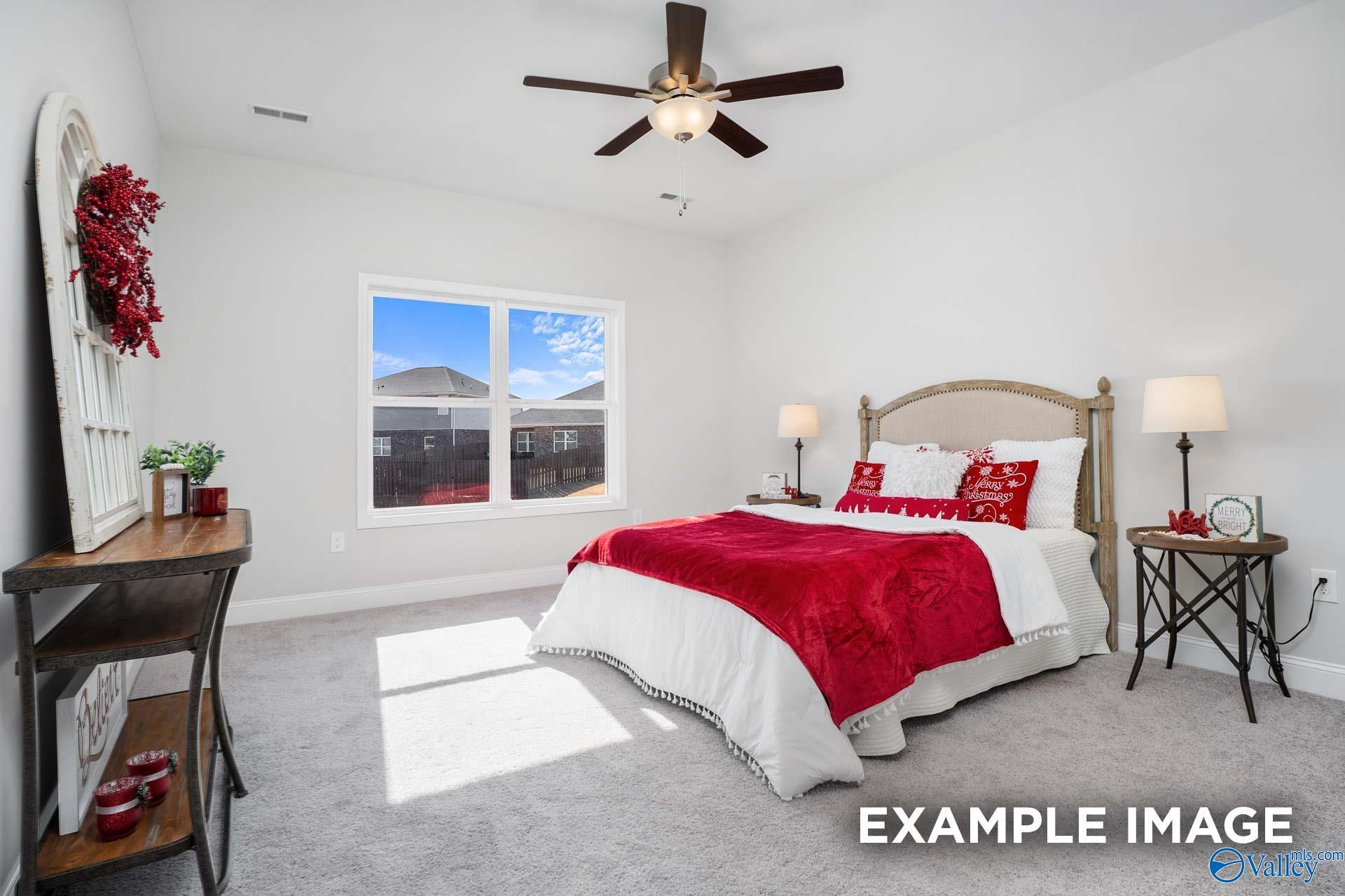Cozy bedroom with red bedding, wooden headboard, ceiling fan, and sunny window in The Daphne D by Davidson Homes, Meridianville, AL