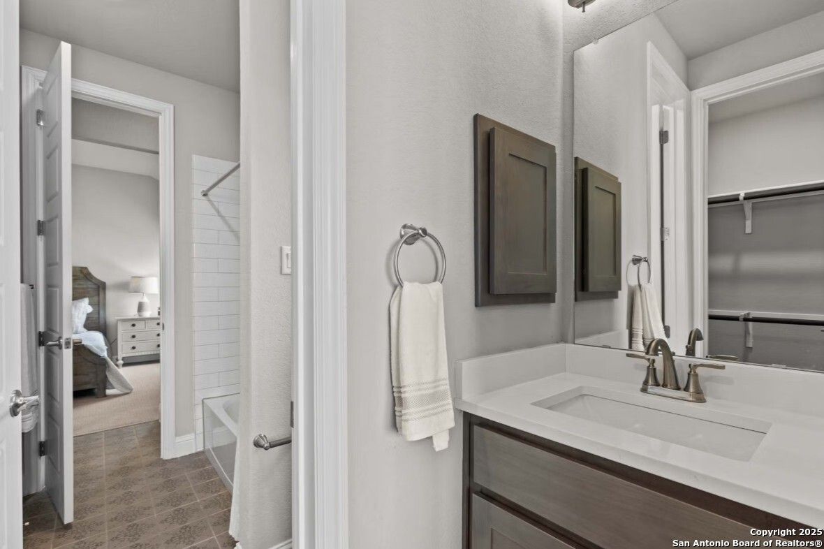 Modern master bathroom with subway tile, single vanity sink, bathtub, and open bedroom door in Davidson Homes The Garner B, Ladera, San Antonio