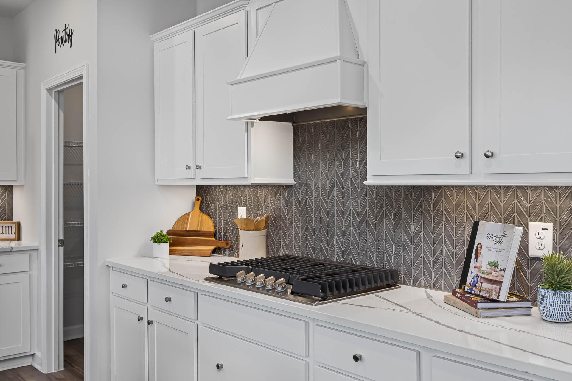Modern white kitchen in Beverly Place Four Oaks NC featuring shaker cabinets, gas cooktop, herringbone backsplash, quartz counters