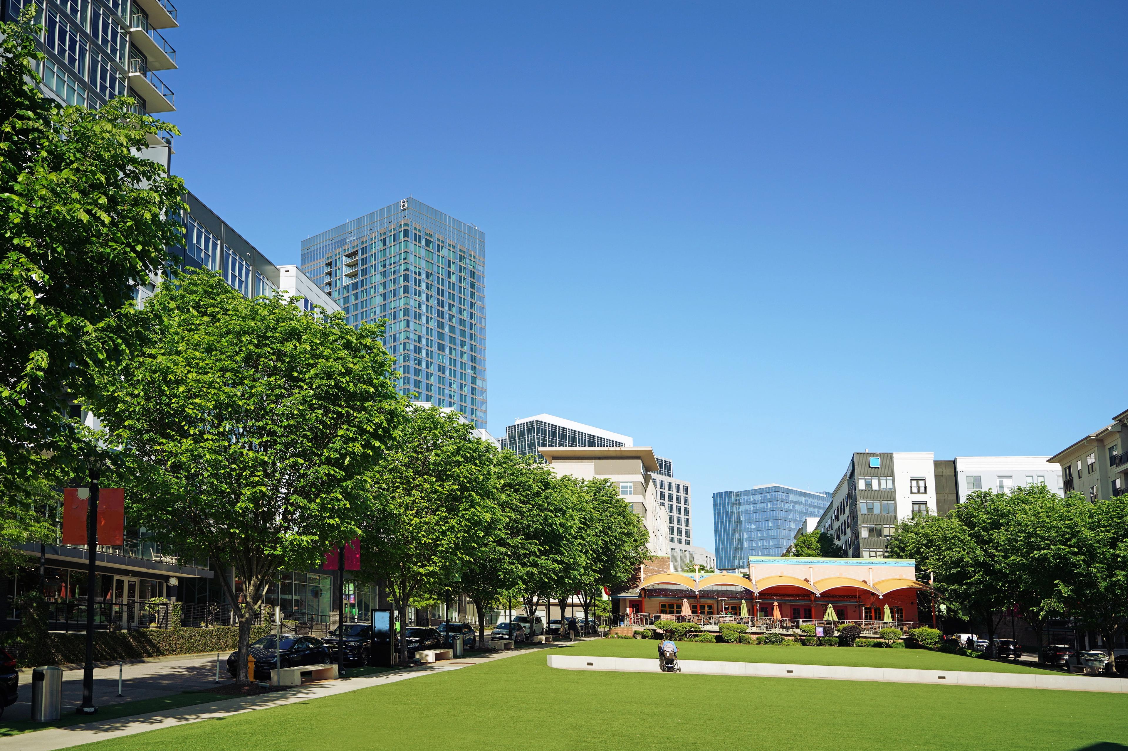 Green park area at Rockport in Wake Forest, NC, featuring lush trees, modern urban architecture, and outdoor seating.