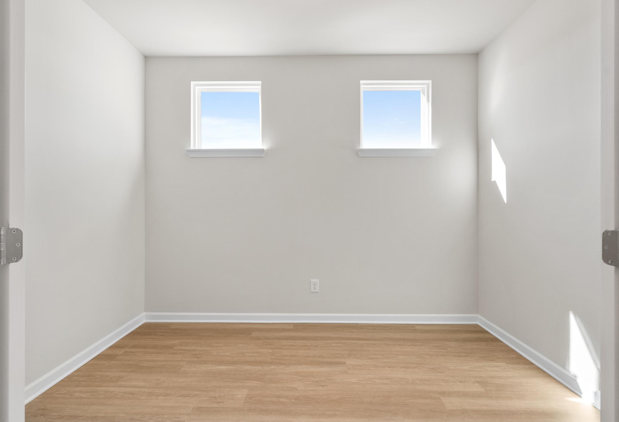 Spacious empty master bedroom in The Dawson C with light gray walls, two sunny windows, hardwood floors, Loganville GA