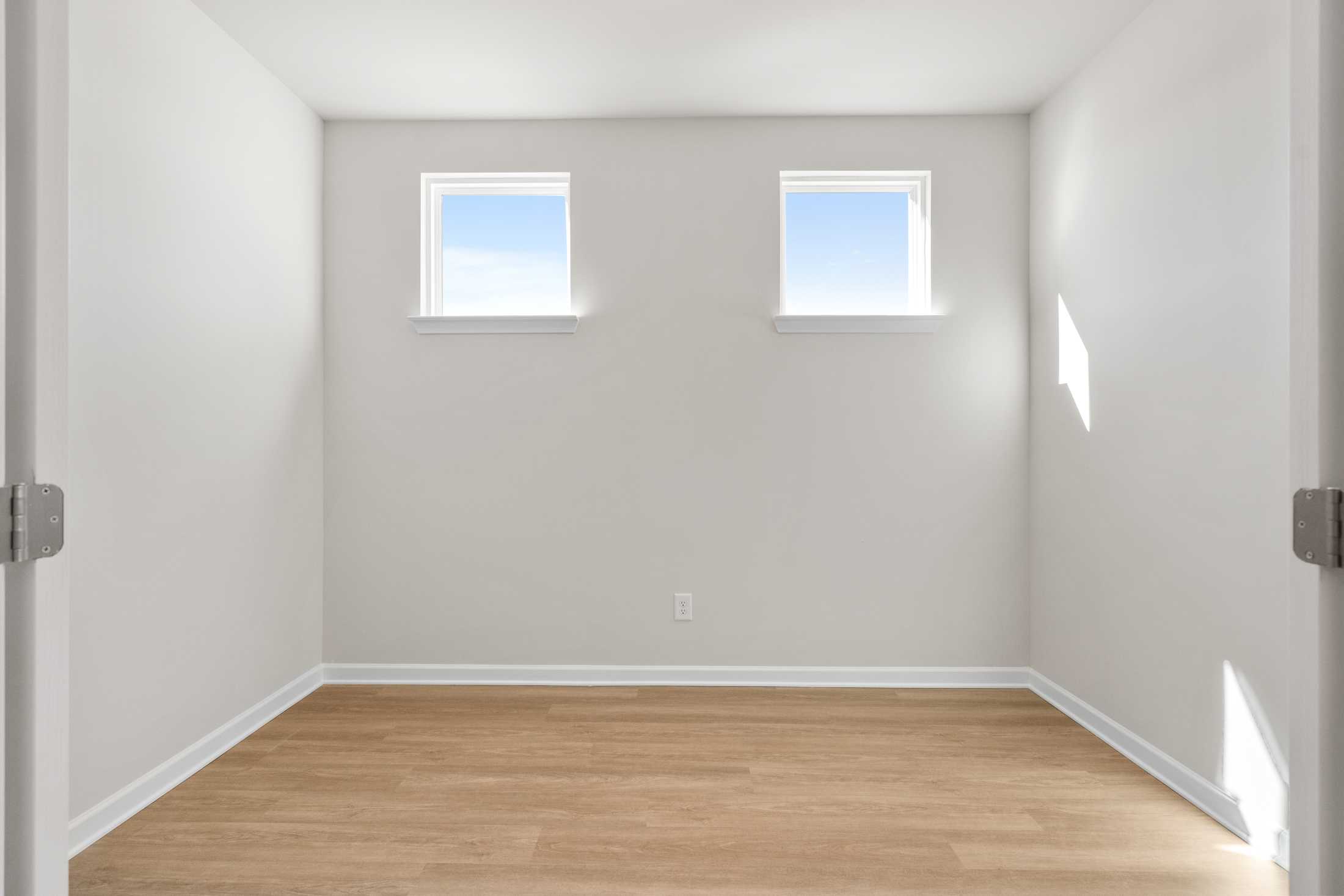 Spacious empty master bedroom in The Dawson C with light gray walls, two sunny windows, hardwood floors, Loganville GA