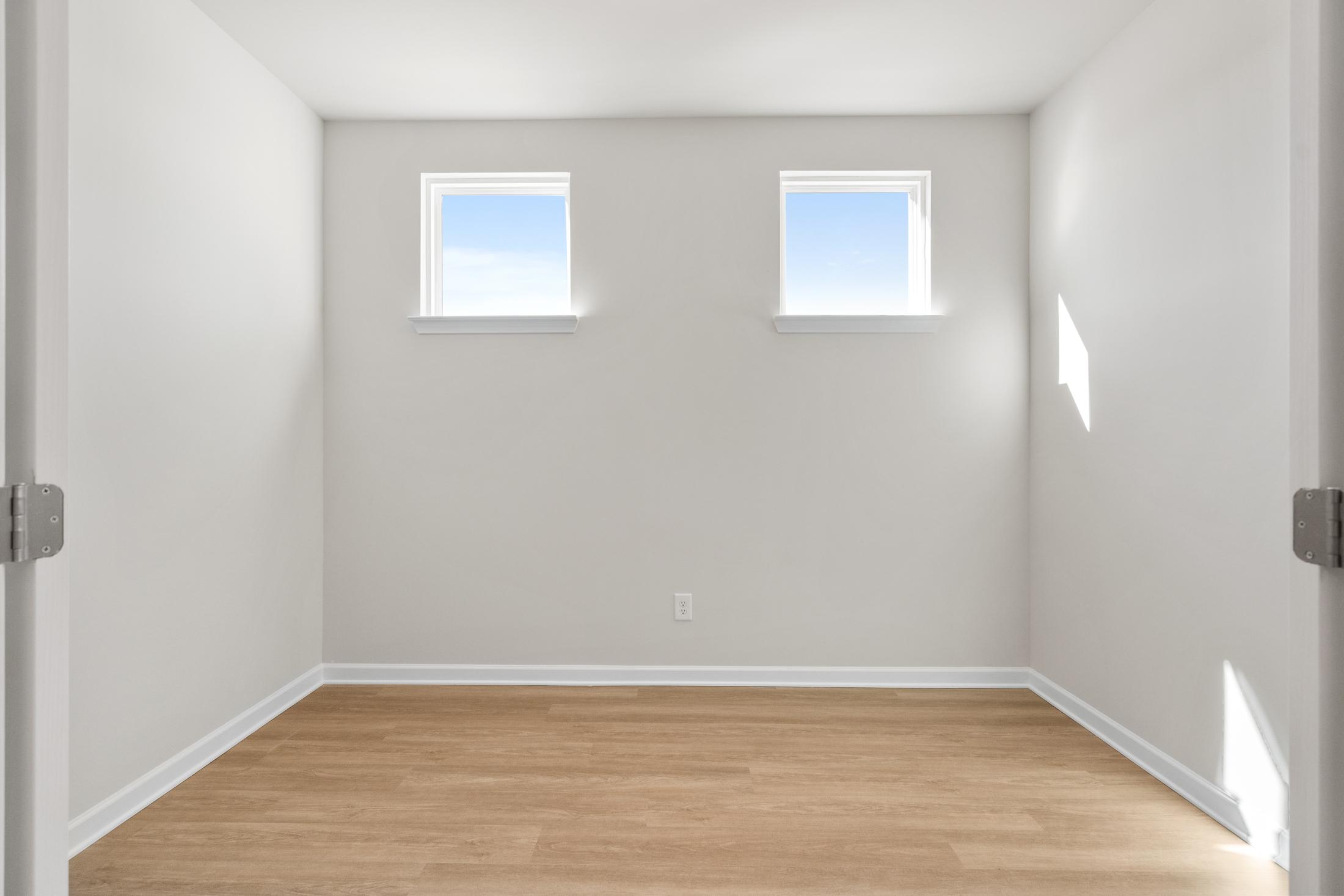 Spacious empty master bedroom in The Dawson C with light gray walls, two sunny windows, hardwood floors, Loganville GA