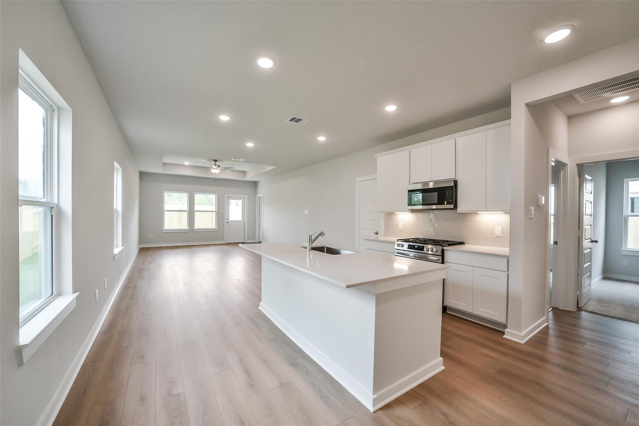 Modern open-concept kitchen with white island, stainless appliances, and hardwood floors in The Frio F home, Conroe, Texas