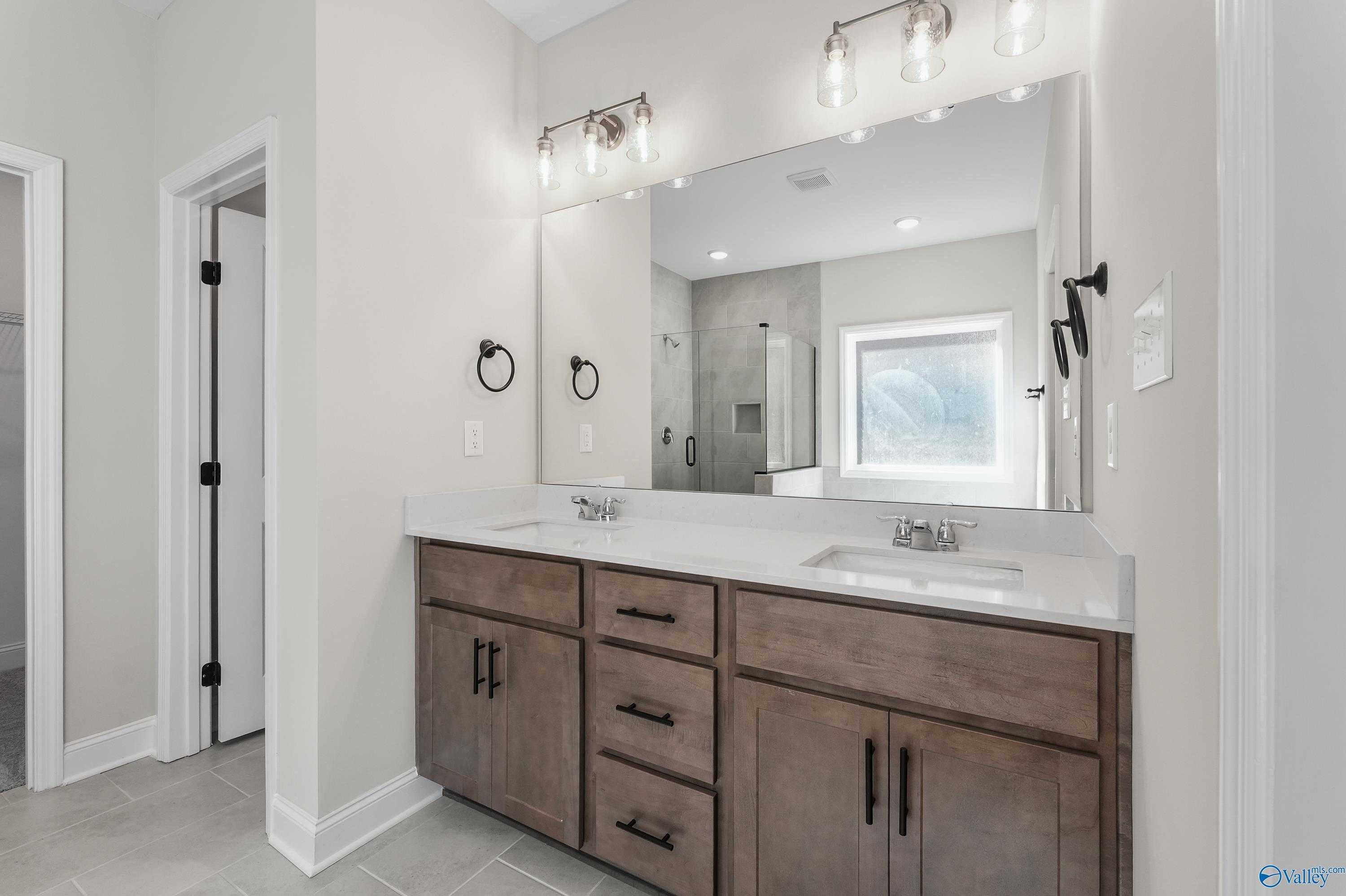 Modern master bathroom featuring double wood vanity, large mirror, glass shower enclosure in Davidson Homes The Montgomery C, Decatur, AL