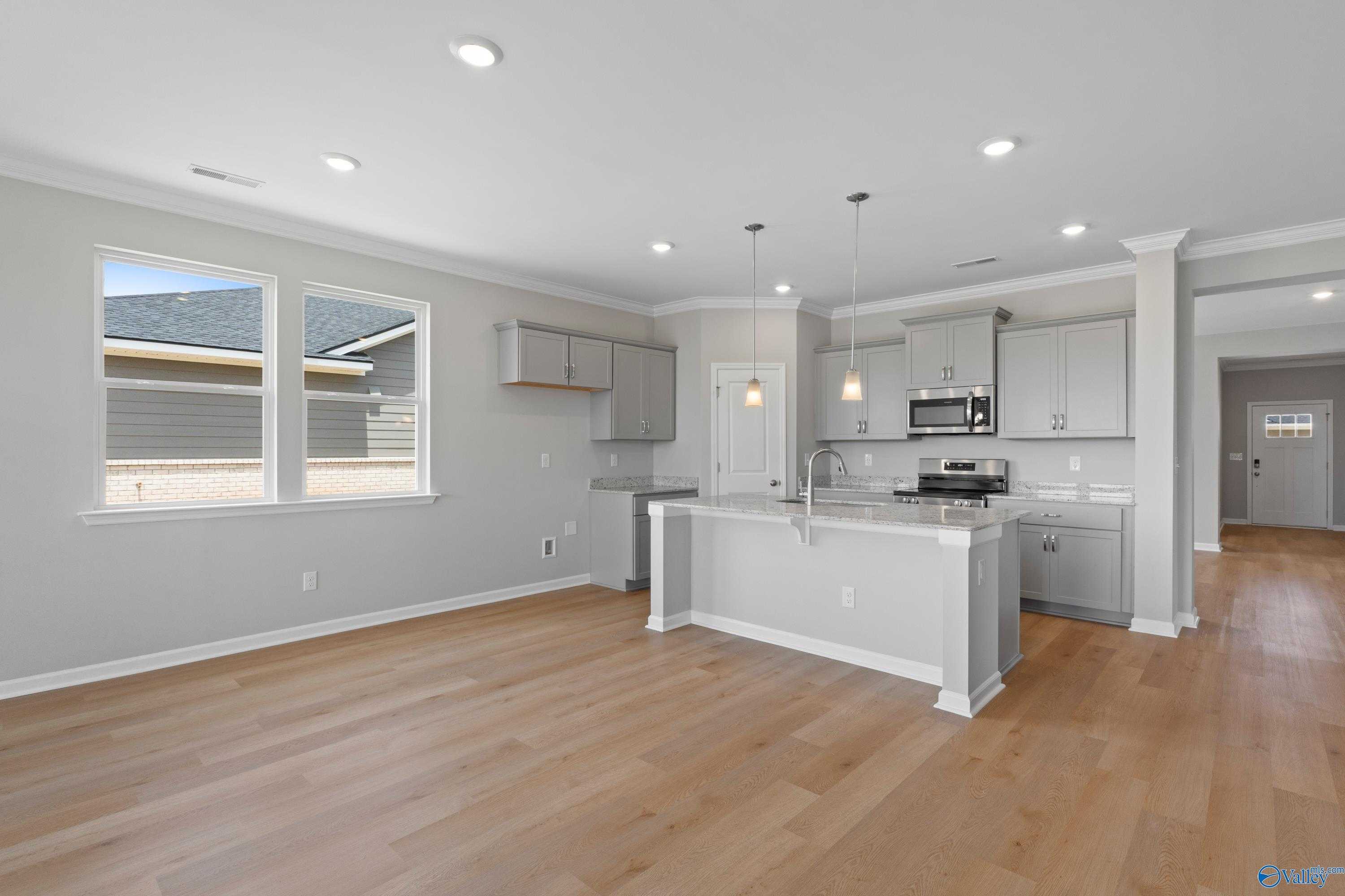 Modern open-concept kitchen with gray shaker cabinets, large center island, stainless microwave, and hardwood floors in Davidson Homes The Orion, Athens AL