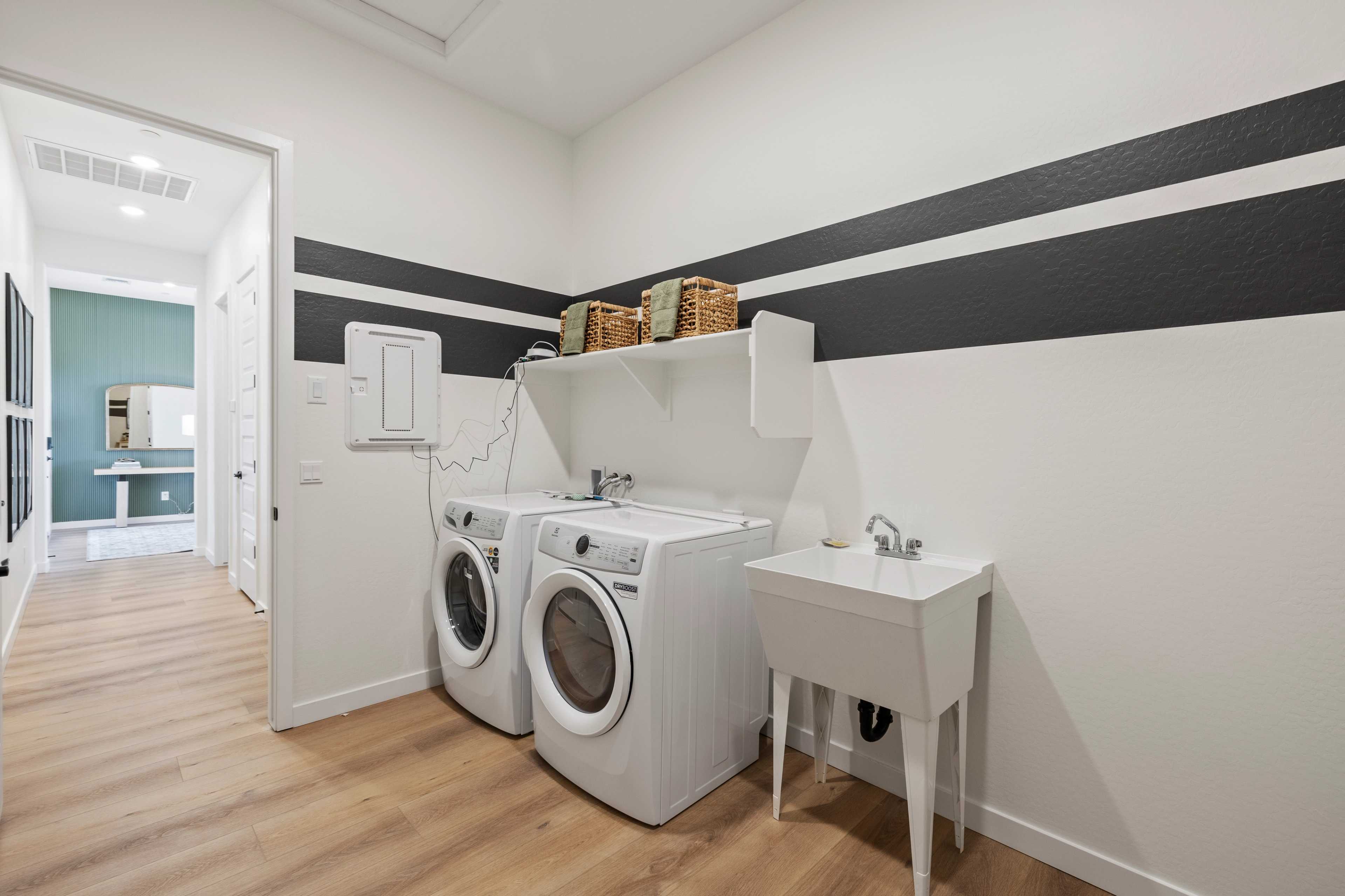 Spacious laundry room at Hidden Hills in Prescott AZ with white washers, utility sink, black striped walls, and hardwood floors